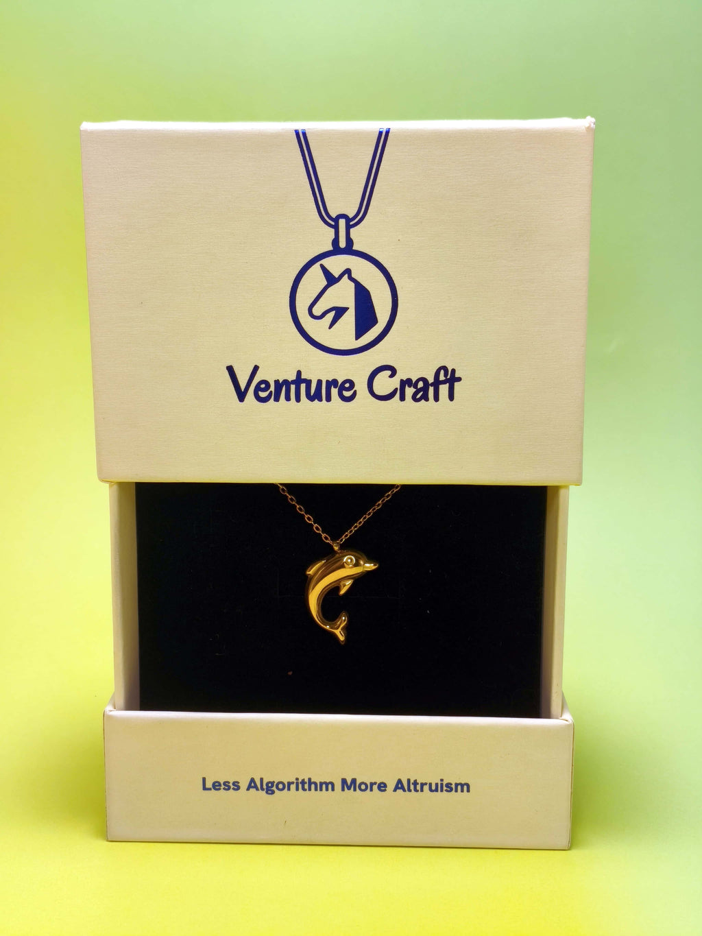 gold necklace with a dolphin pendant in a Venture Craft gift box on a green background