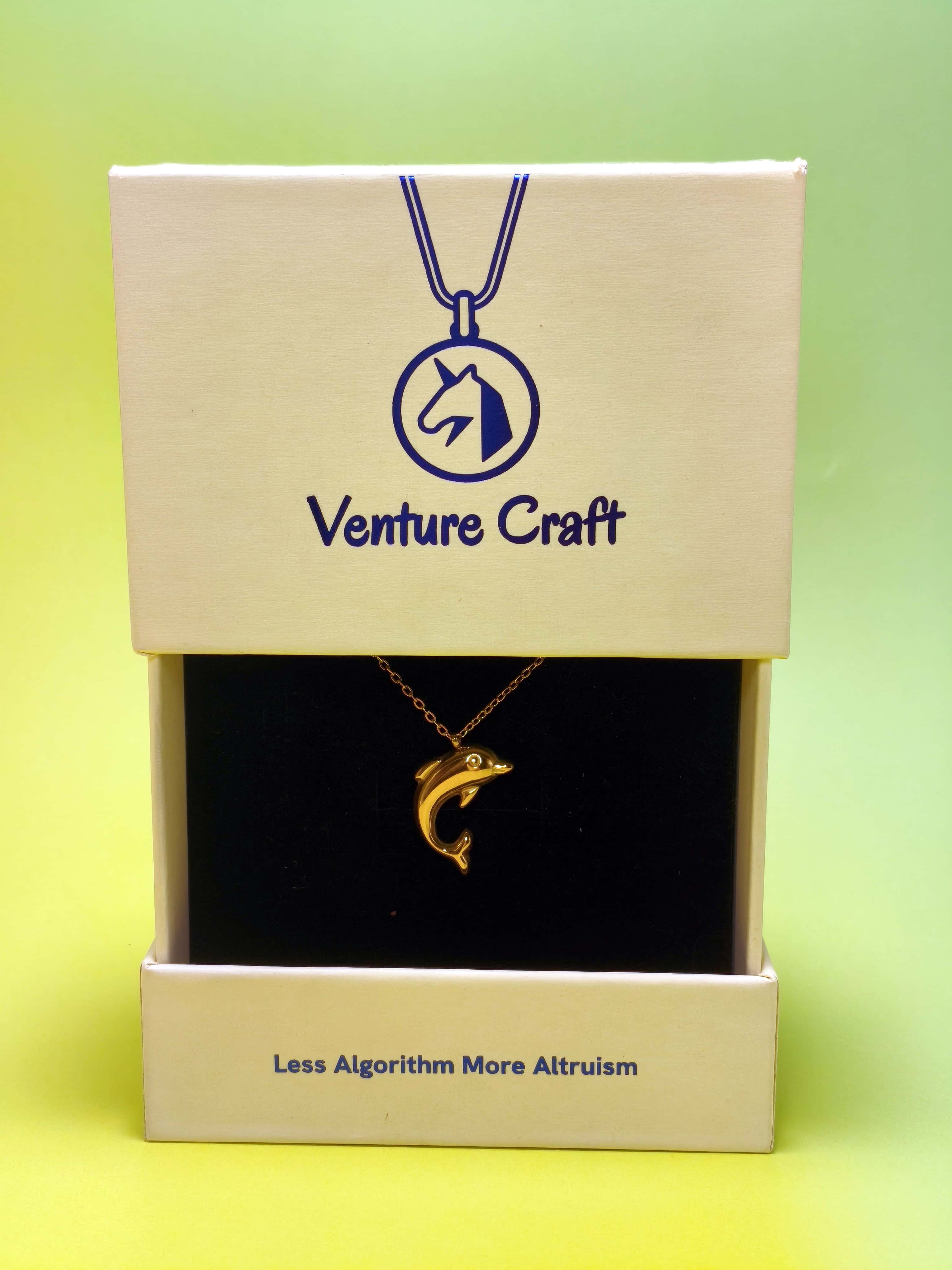 gold necklace with a dolphin pendant in a Venture Craft gift box on a green background