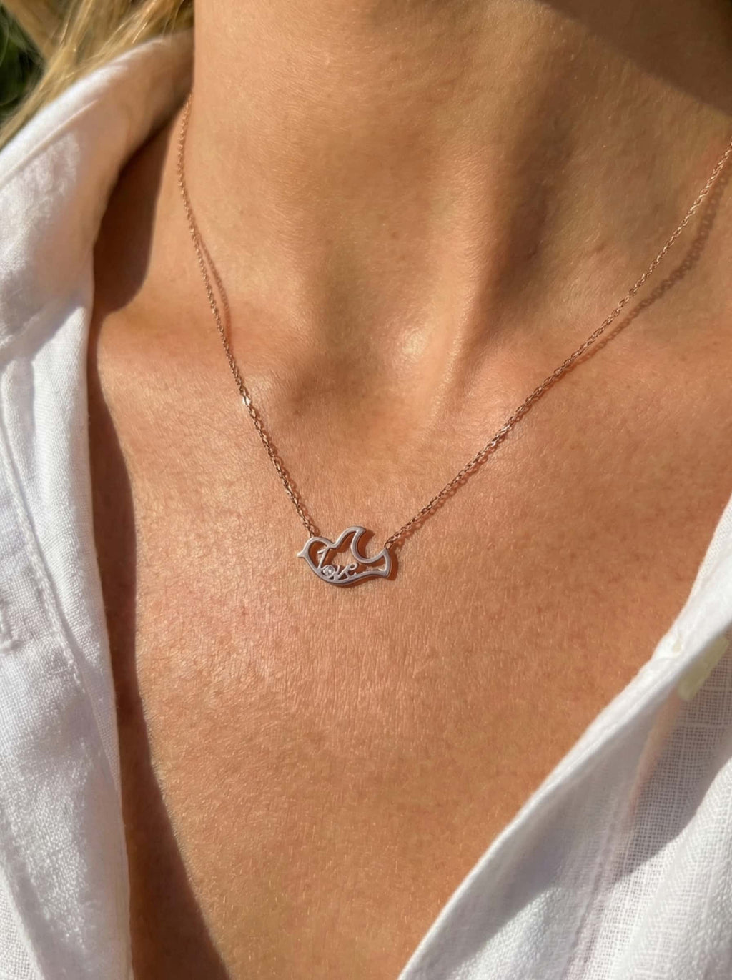 Necklace with a dove-shaped pendant on a person wearing a white shirt.