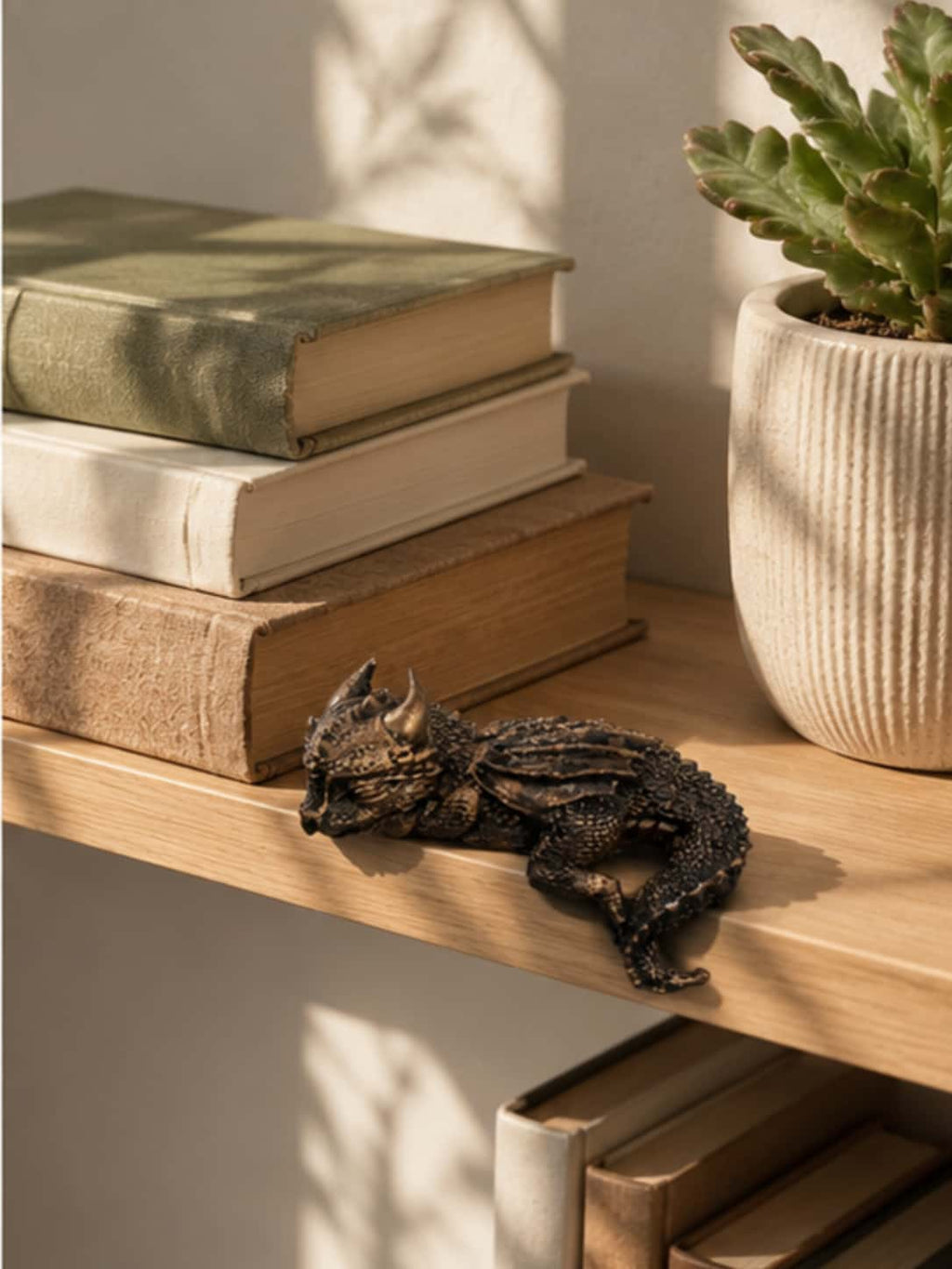 Sleeping dragon statue displayed as cozy dragon home decor on a wooden shelf next to a potted succulent and books