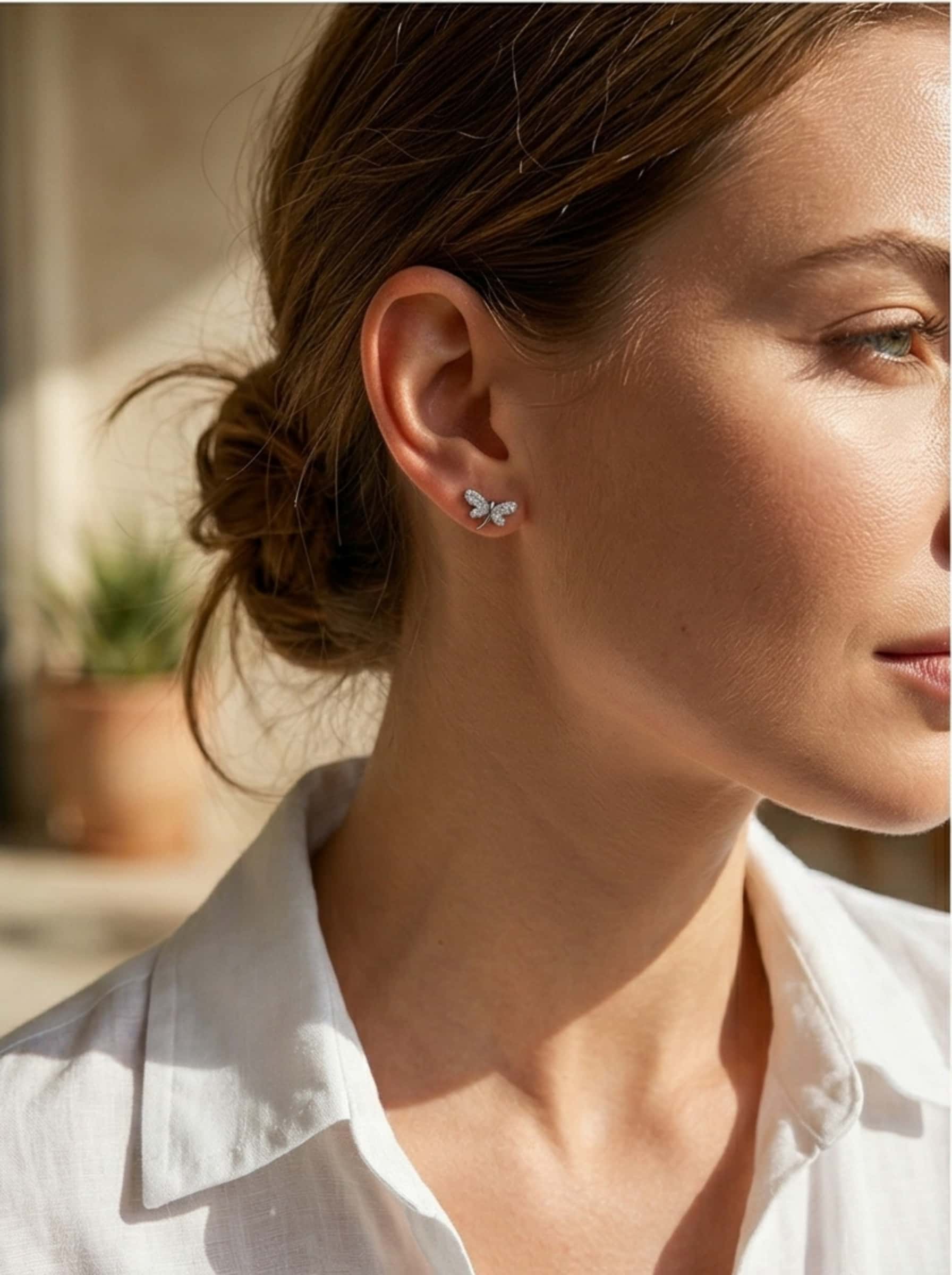 Lifestyle portrait of a woman styling chic dragonfly earrings with a classic white shirt.