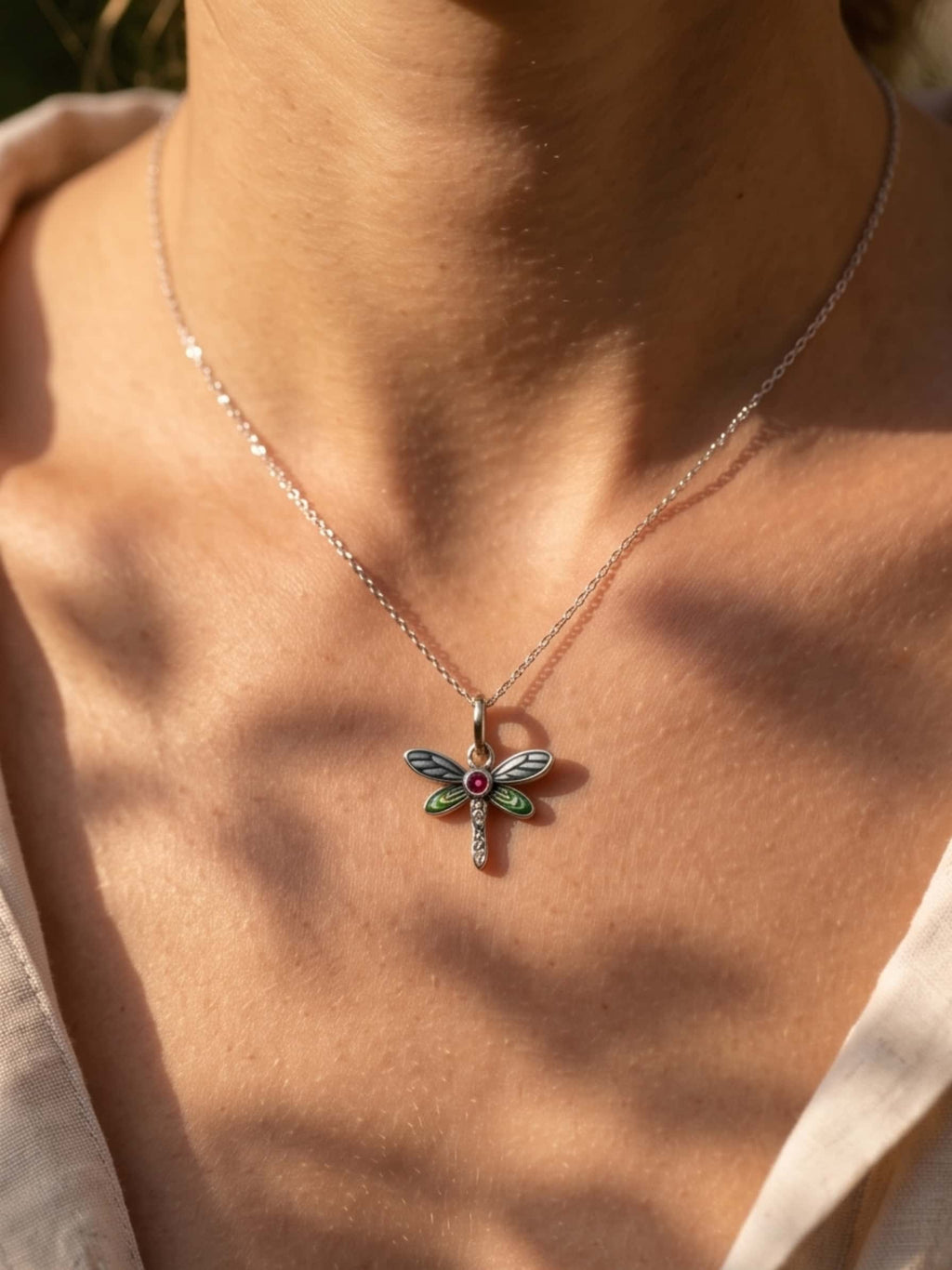 Close-up of a woman wearing a dragonfly pendant necklace under natural sunlight, highlighting the intricate green enamel wings and AAA cubic zirconia stones on the collarbone