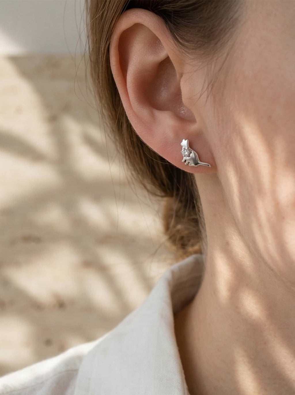 A woman in a crisp white shirt wearing subtle and elegant cat earrings, showcasing an ideal gift for cat lovers