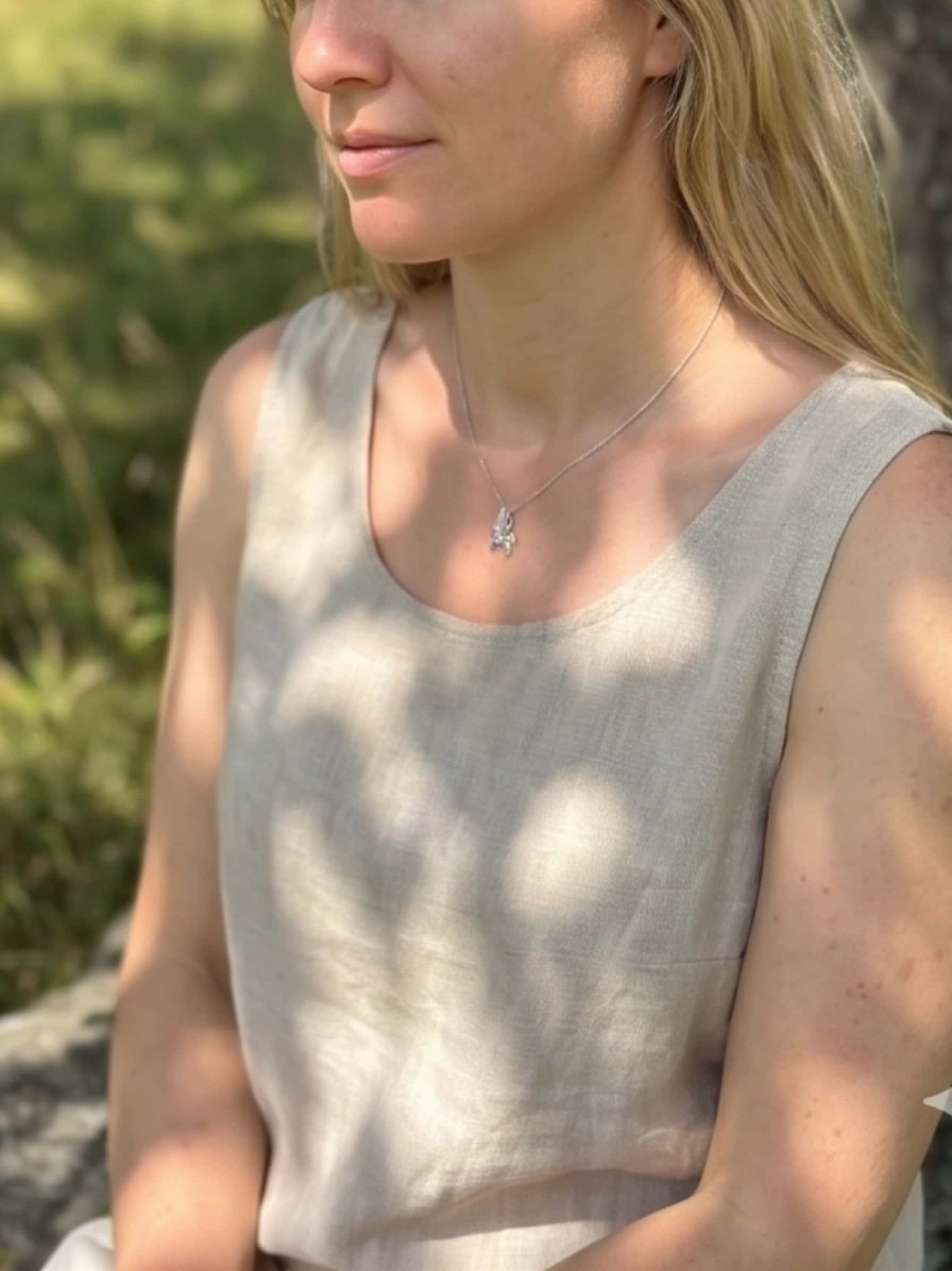 Woman resting outdoors under dappled tree shadows while wearing a detailed silver unicorn necklace, conveying a sense of calm and companionship