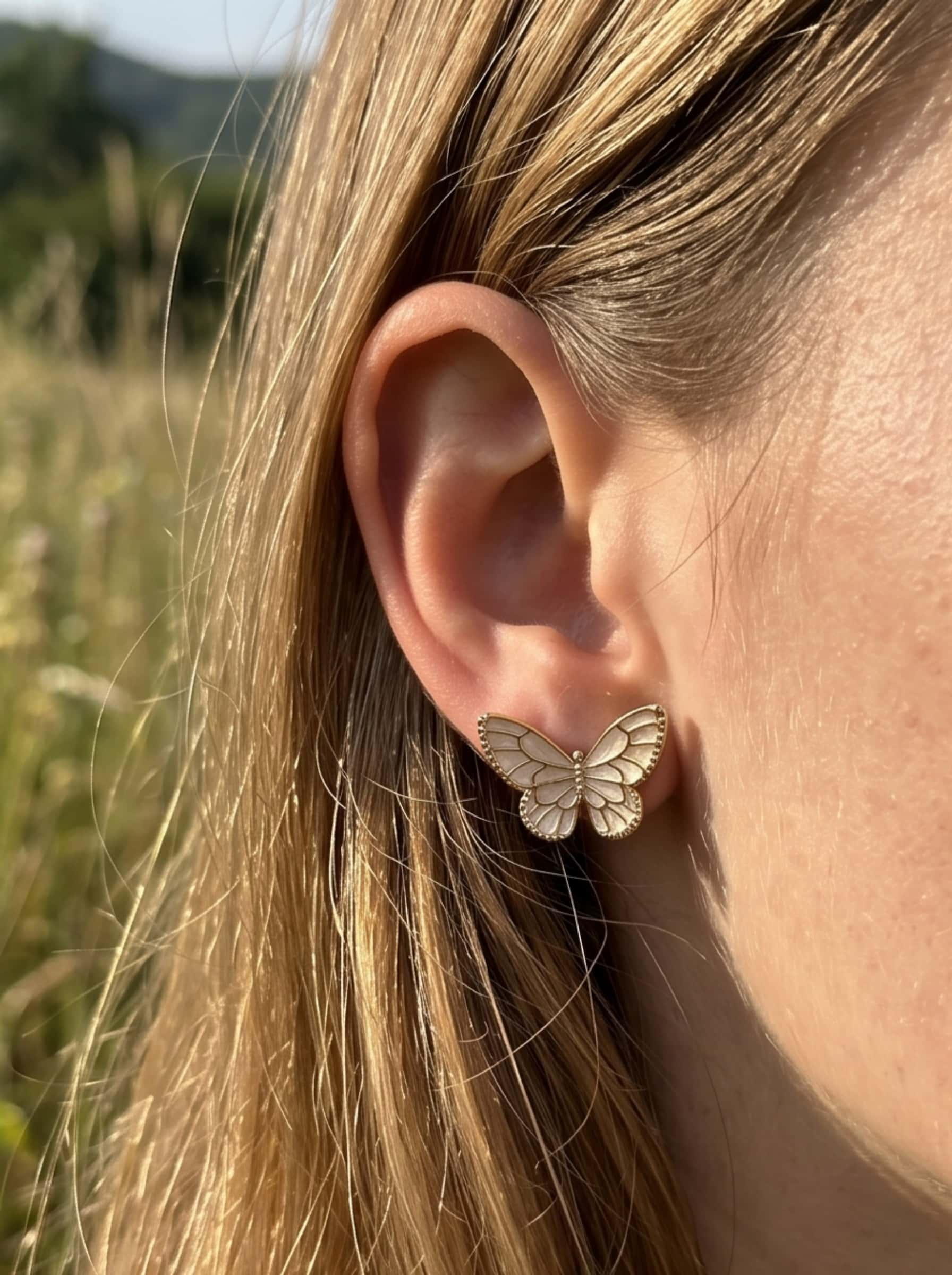 Close-up view of a model wearing a radiant gold butterfly earring in natural outdoor sunlight, highlighting the intricate enamel work and clean girl aesthetic