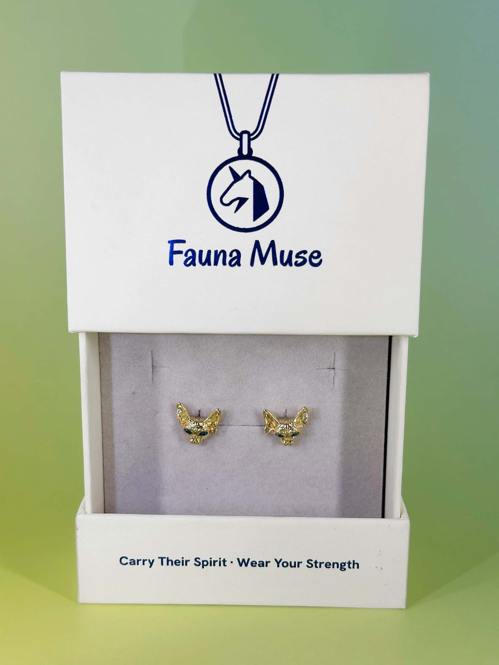 Fauna Muse gold cat stud earrings with green gemstone eyes displayed in a white branded jewelry gift box