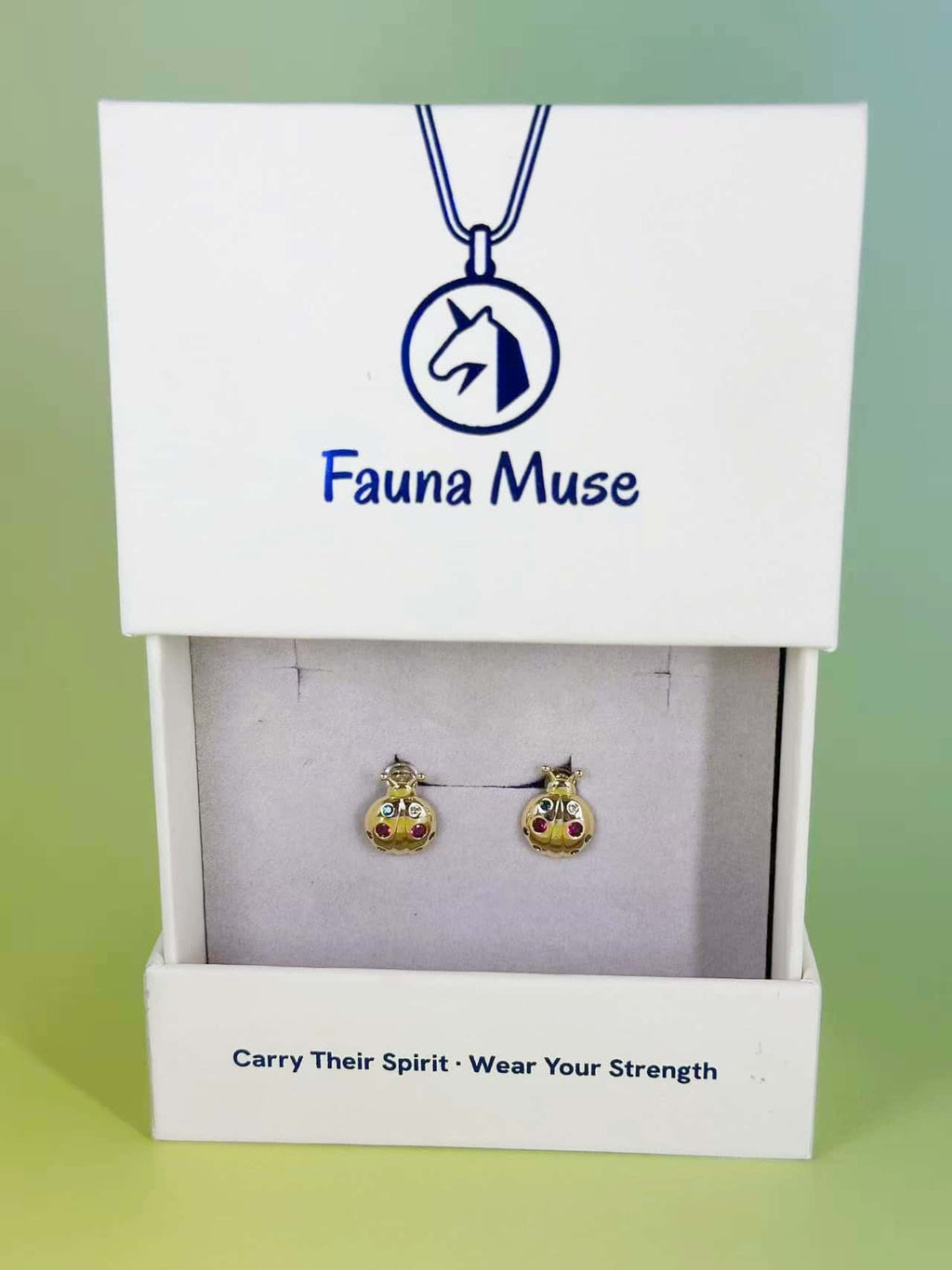 Fauna Muse gold ladybug stud earrings with colorful gemstone spots displayed in a white branded jewelry gift box