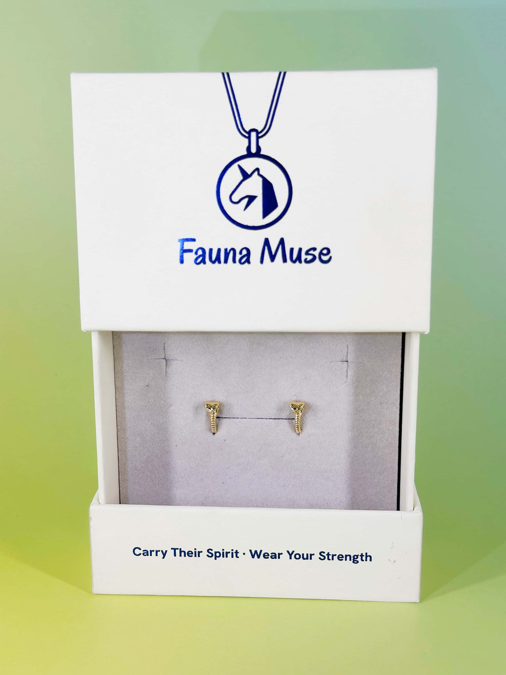 Fauna Muse gold snake huggie hoop earrings with green gemstone eyes displayed in a white branded jewelry gift box