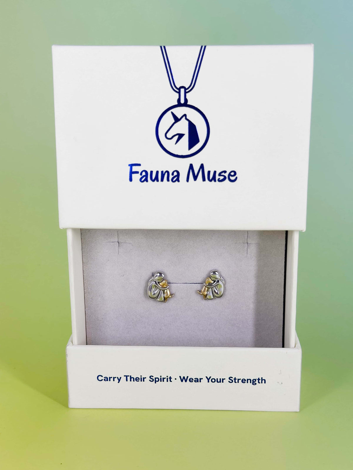 Fauna Muse two-tone silver and gold person hugging dog stud earrings displayed in a white branded jewelry gift box