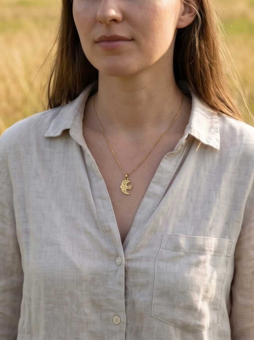 A female model wearing the delicate gold bird necklace paired with a natural linen shirt in a sunlit autumn field