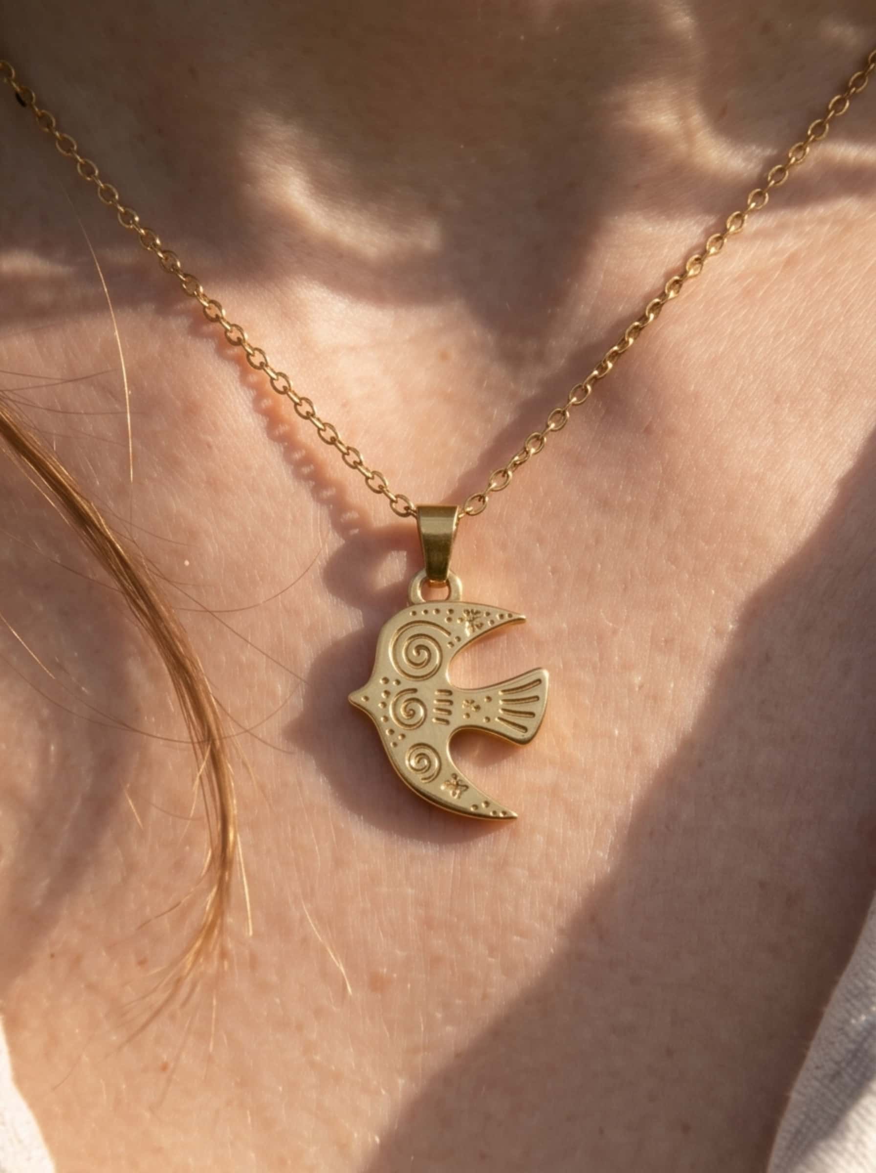 Macro close-up shot of the engraved bird necklace pendant showcasing the detailed stars and spirals craftsmanship against the skin