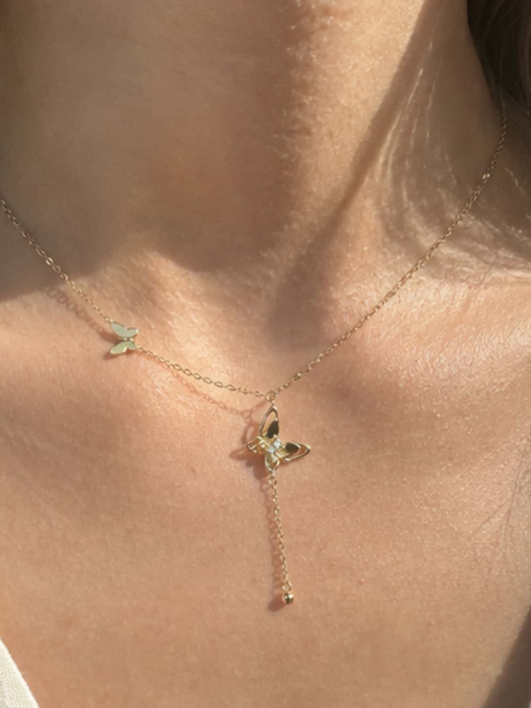 Close-up macro shot of the gold butterfly necklace gold pendant on a woman's neck, highlighting the cubic zirconia stones catching the natural sunlight