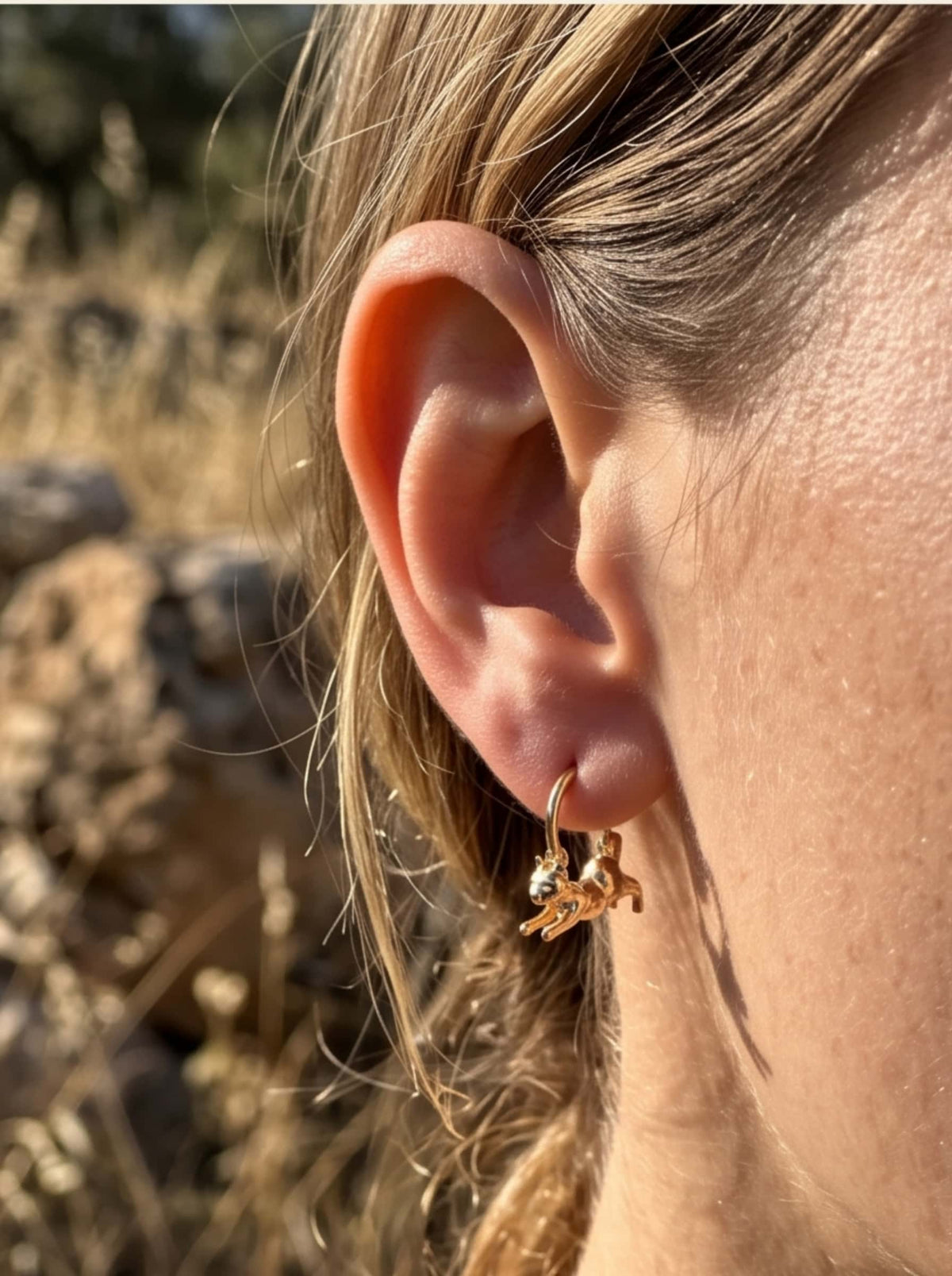 Close-up shot of a dainty 18K gold cat hoop earring worn on the ear in natural sunlight