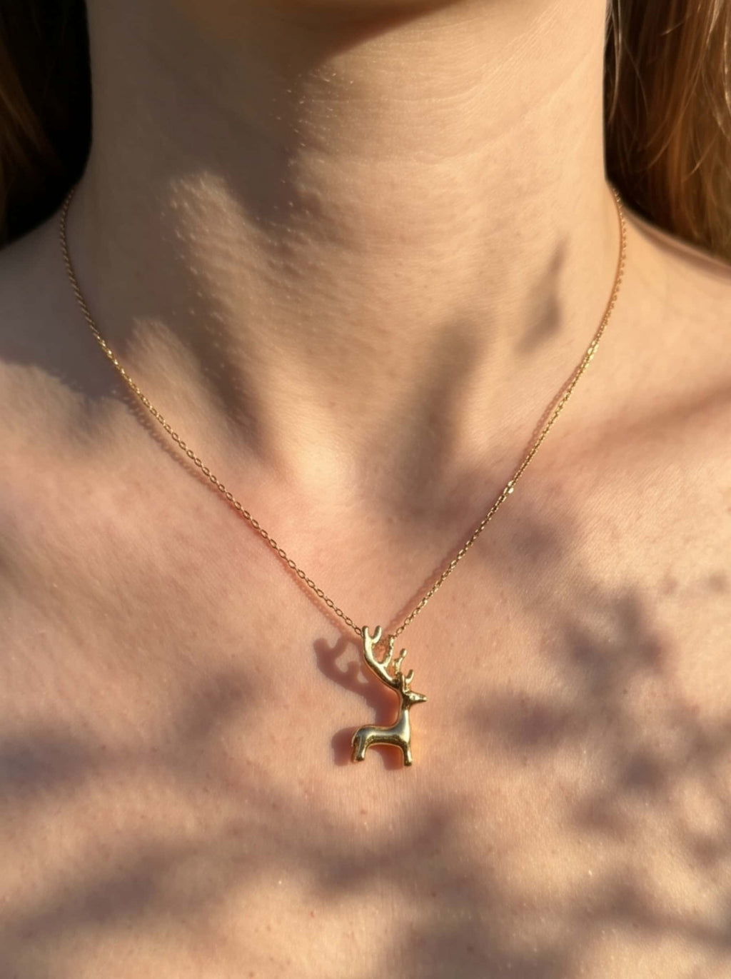 Close-up view of the 18K gold plated deer necklace worn on collarbone in soft natural sunlight