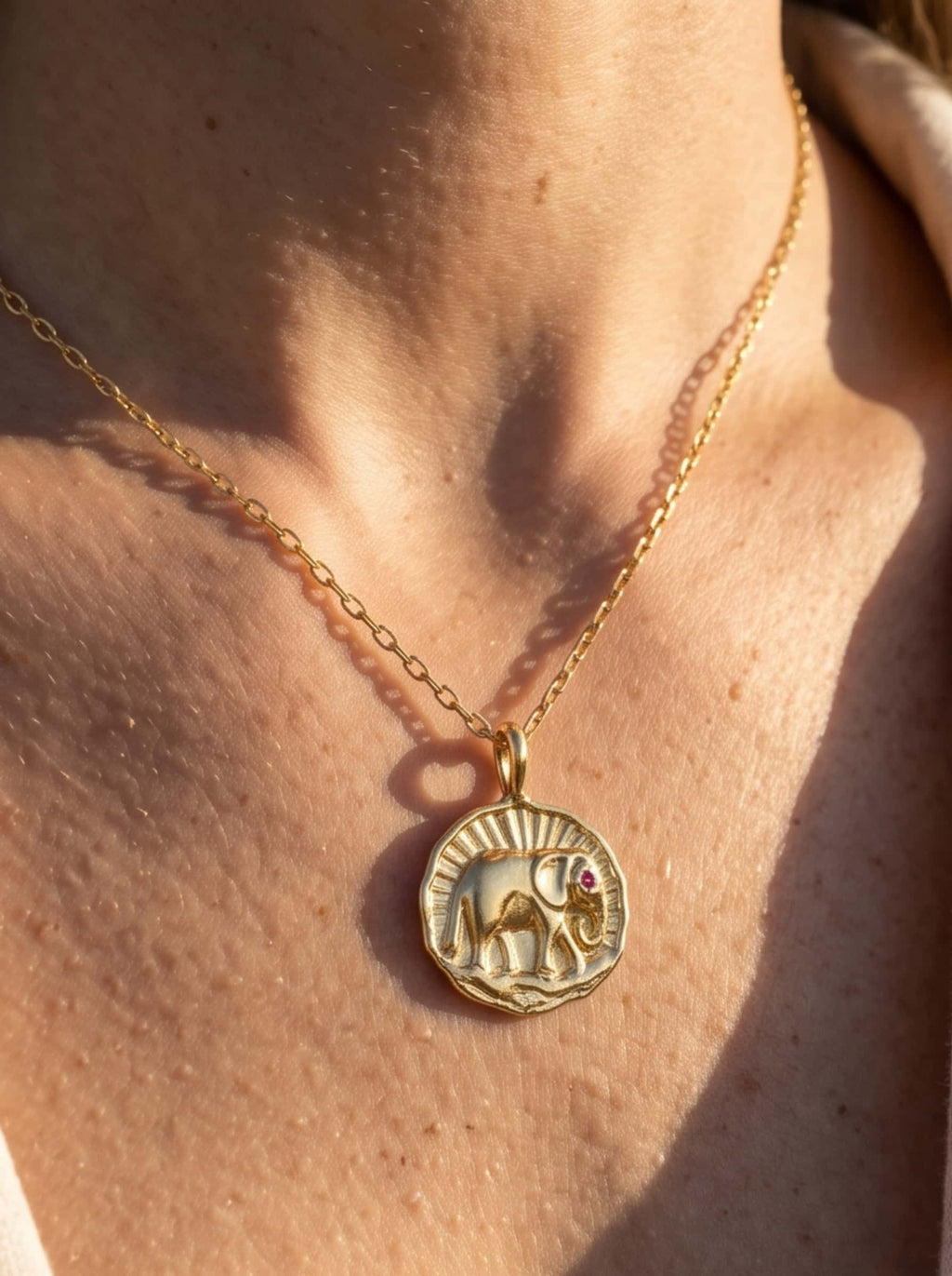 Close-up of a model wearing the gold elephant necklace in warm golden hour sunlight, highlighting the intricate medallion pendant