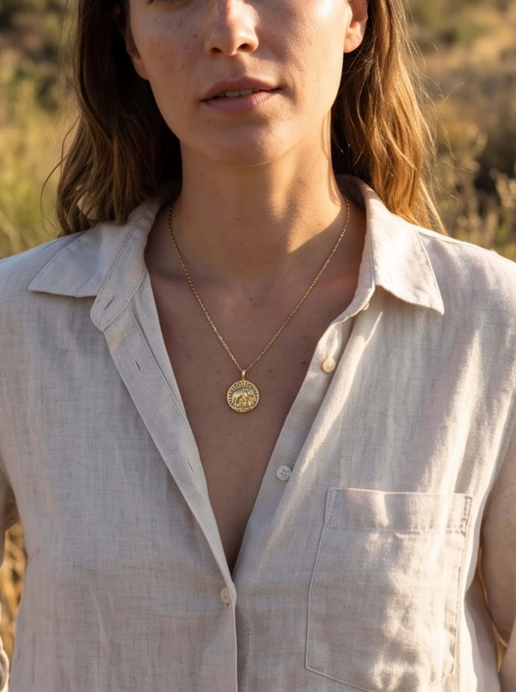 A woman wearing the gold elephant pendant necklace with a relaxed beige linen shirt, showing a natural and organic lifestyle style
