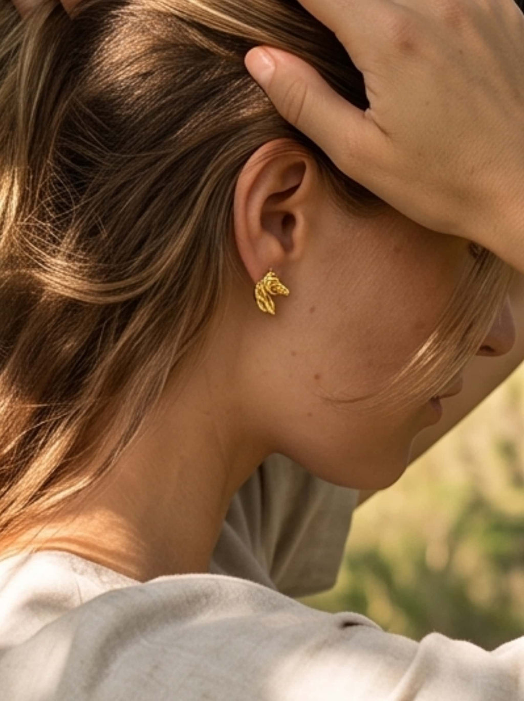 Model styling 18K gold horse earrings with neutral summer linen attire in a field