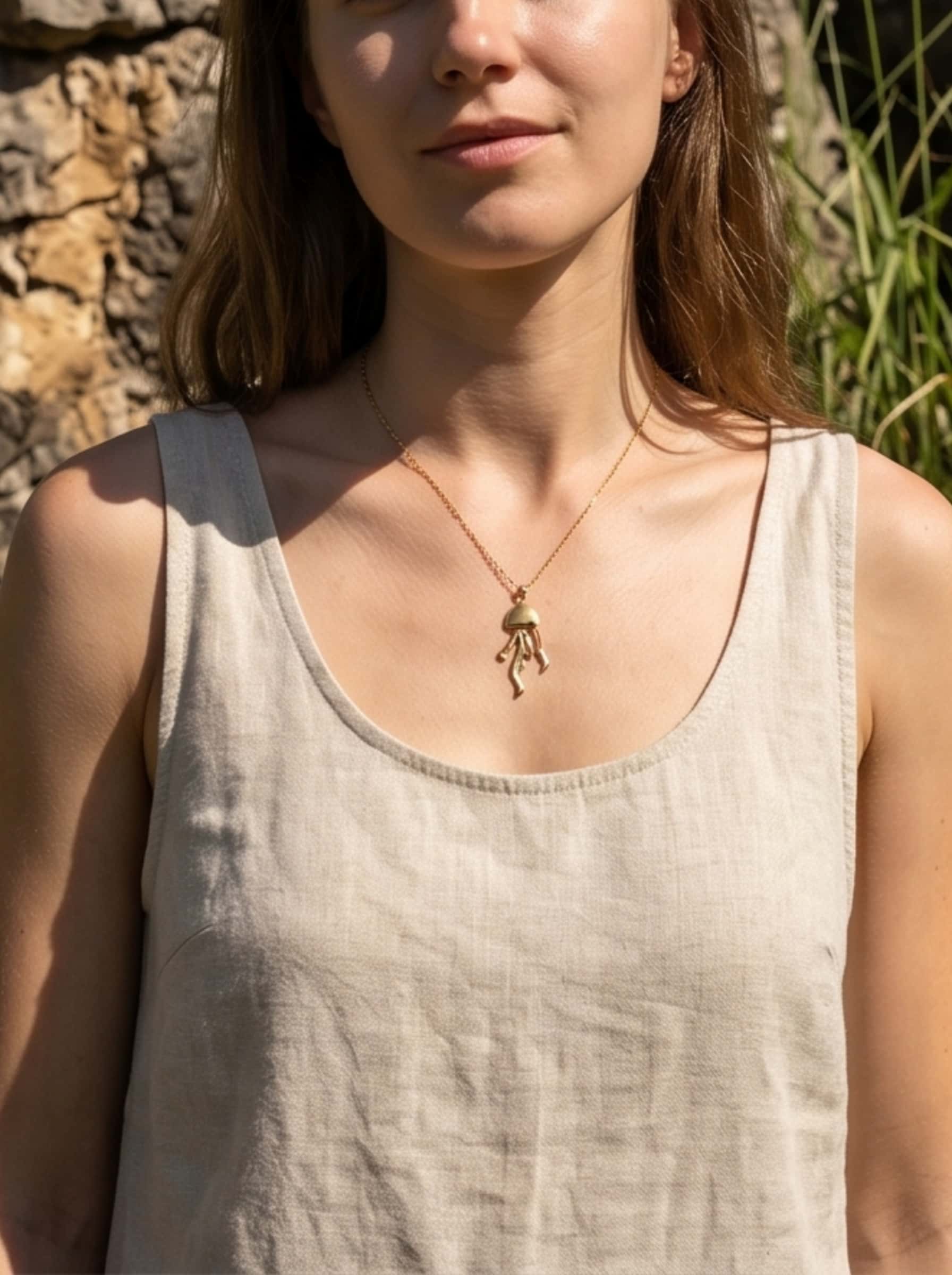 A female model wearing the minimalist golden jellyfish necklace, paired with a beige linen top in warm, natural outdoor sunlight