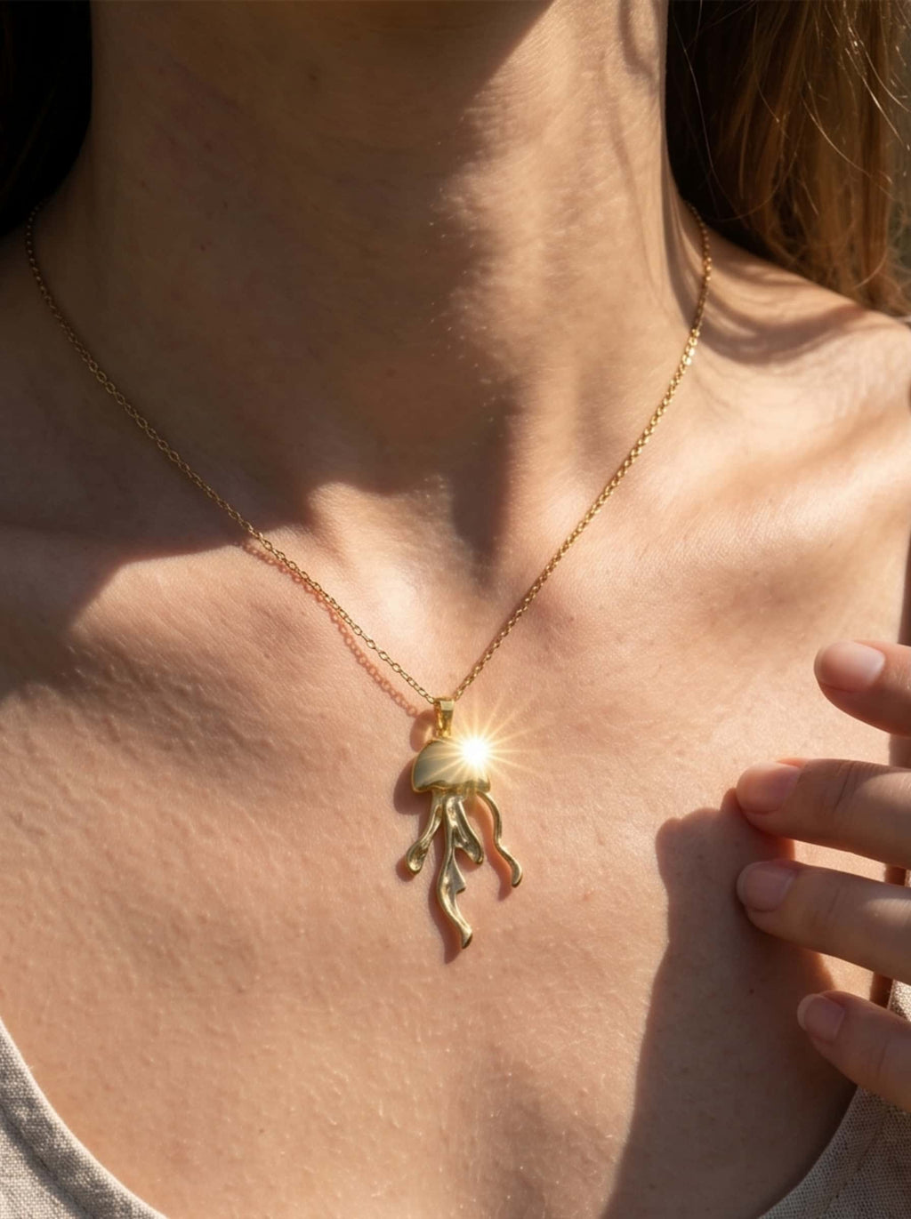 Macro detailed shot of the 18K gold jellyfish necklace pendant catching a brilliant sun flare reflection on a model's neckline