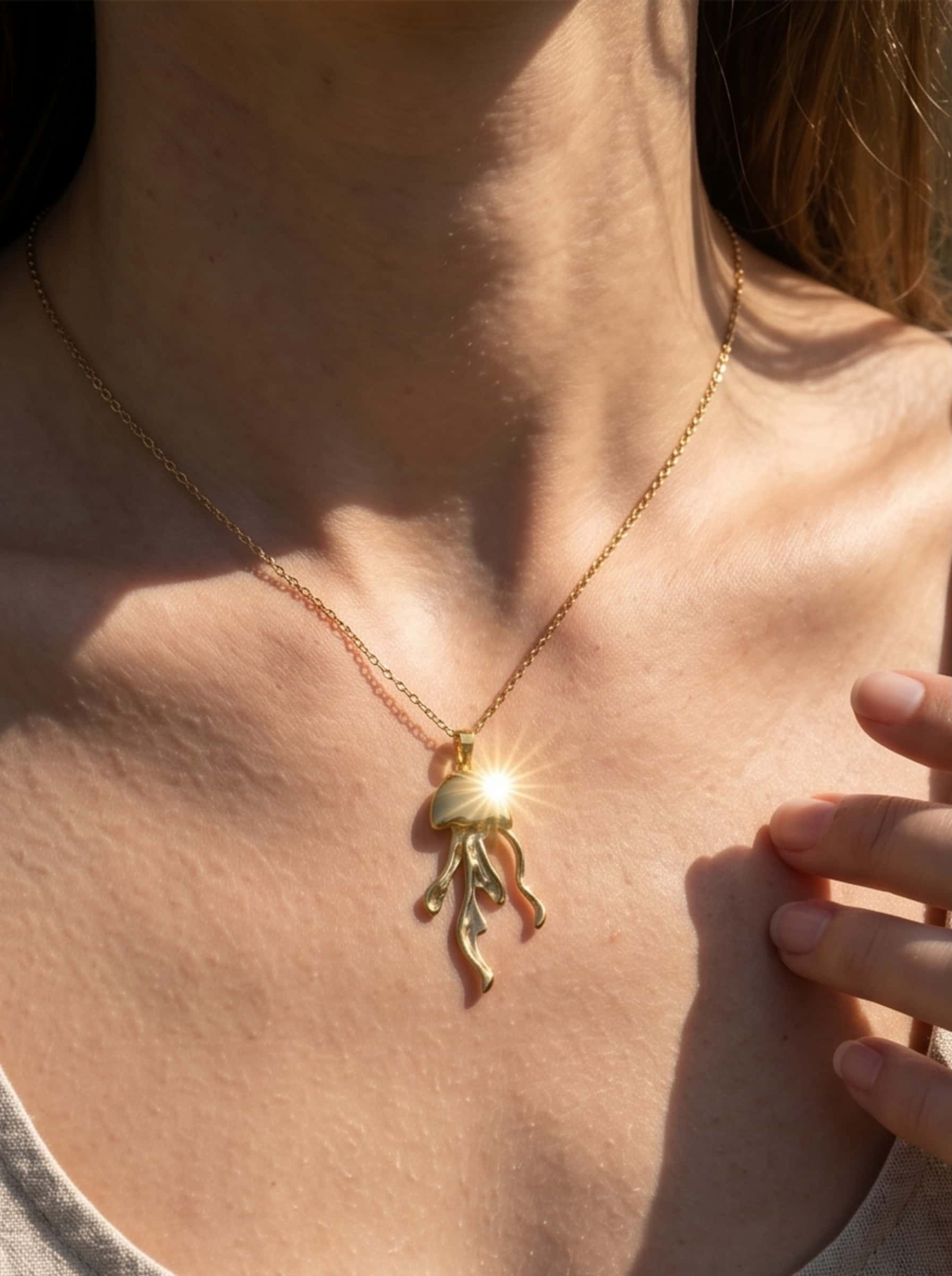 Macro detailed shot of the 18K gold jellyfish necklace pendant catching a brilliant sun flare reflection on a model's neckline