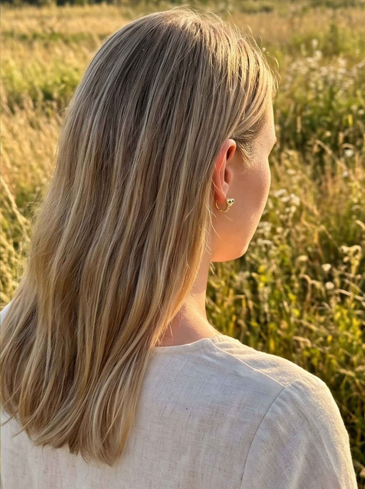 Side profile view of model styling gold snake earrings with a casual neutral outfit outdoors