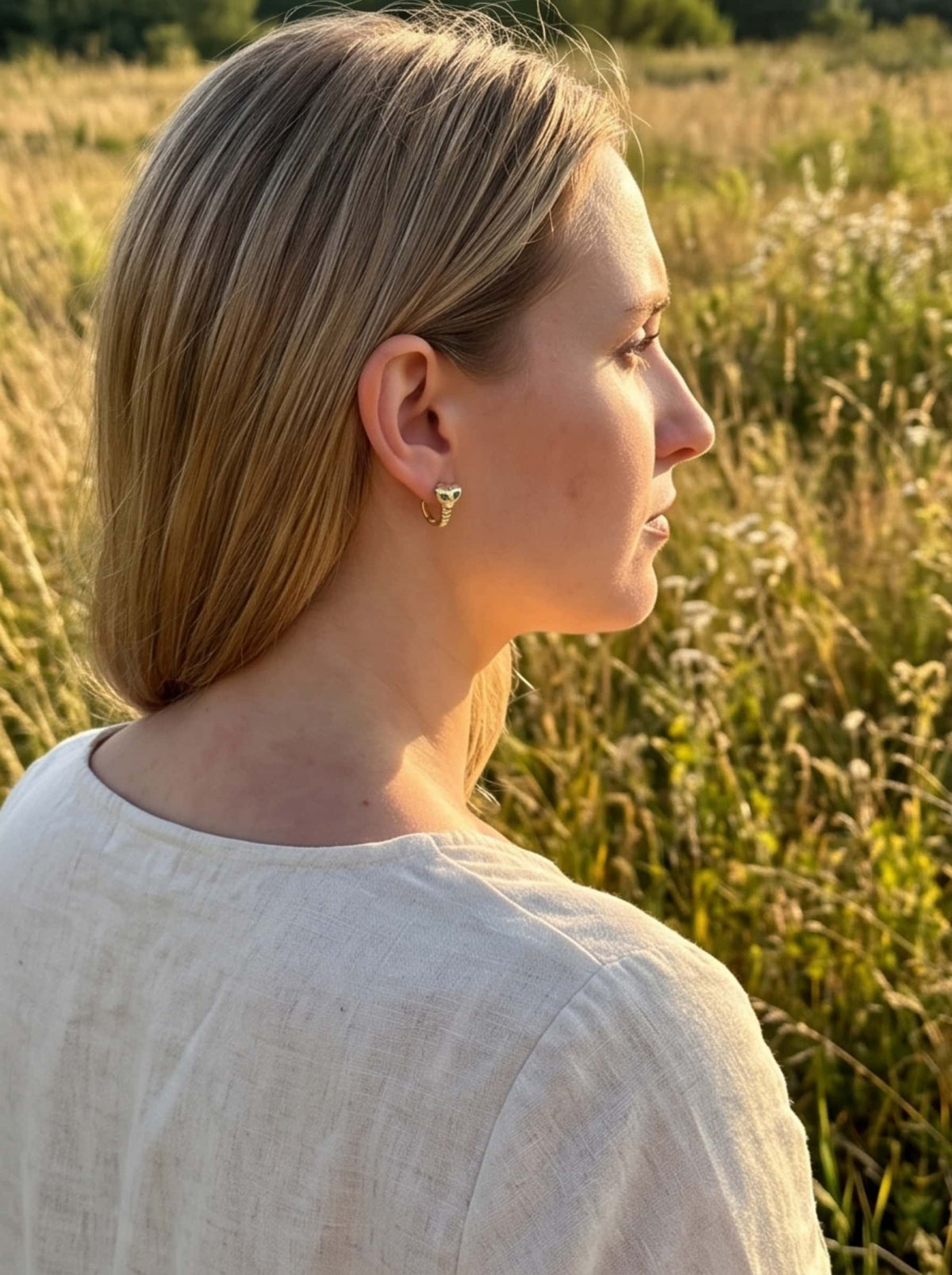 Model wearing 18K gold snake earrings in natural golden hour outdoor sunlight