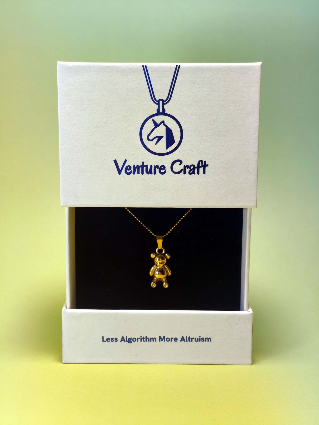 gold teddy bear pendant necklace in a Venture Craft gift box on a gradient background
