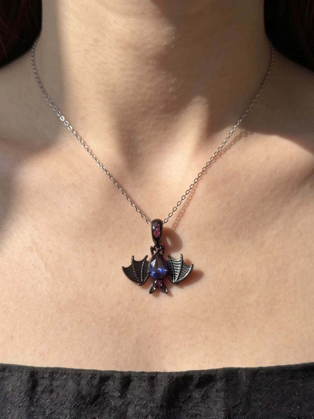 Detailed view of a gothic bat necklace resting beautifully on a woman's collarbone in natural sunlight