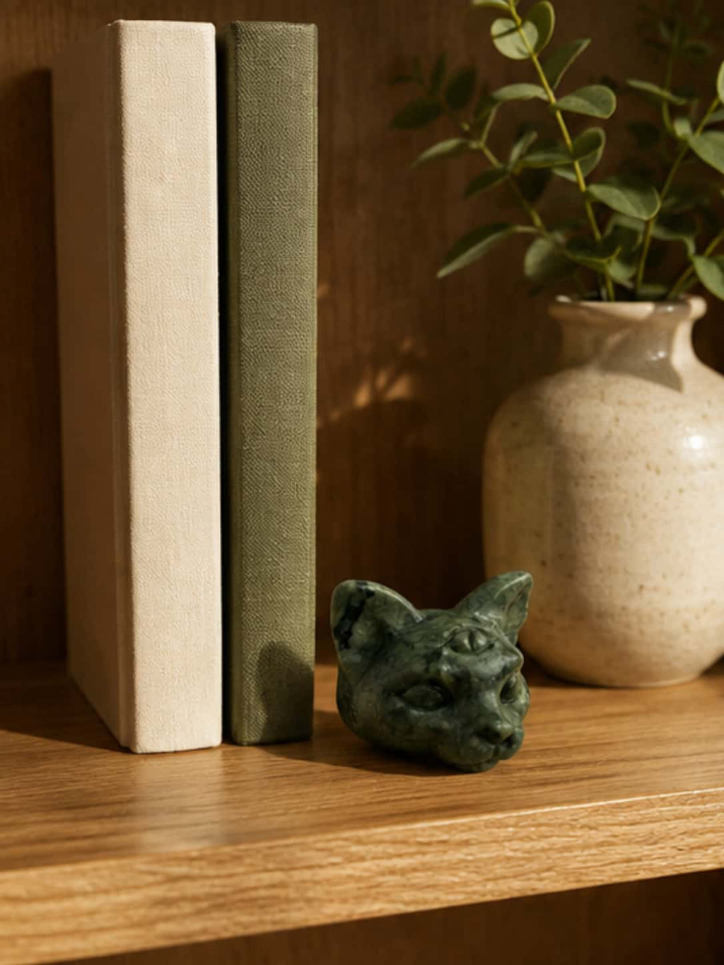 Aesthetic cat decor crystal figurine nestled between clothbound vintage books and a ceramic vase on a wooden shelf