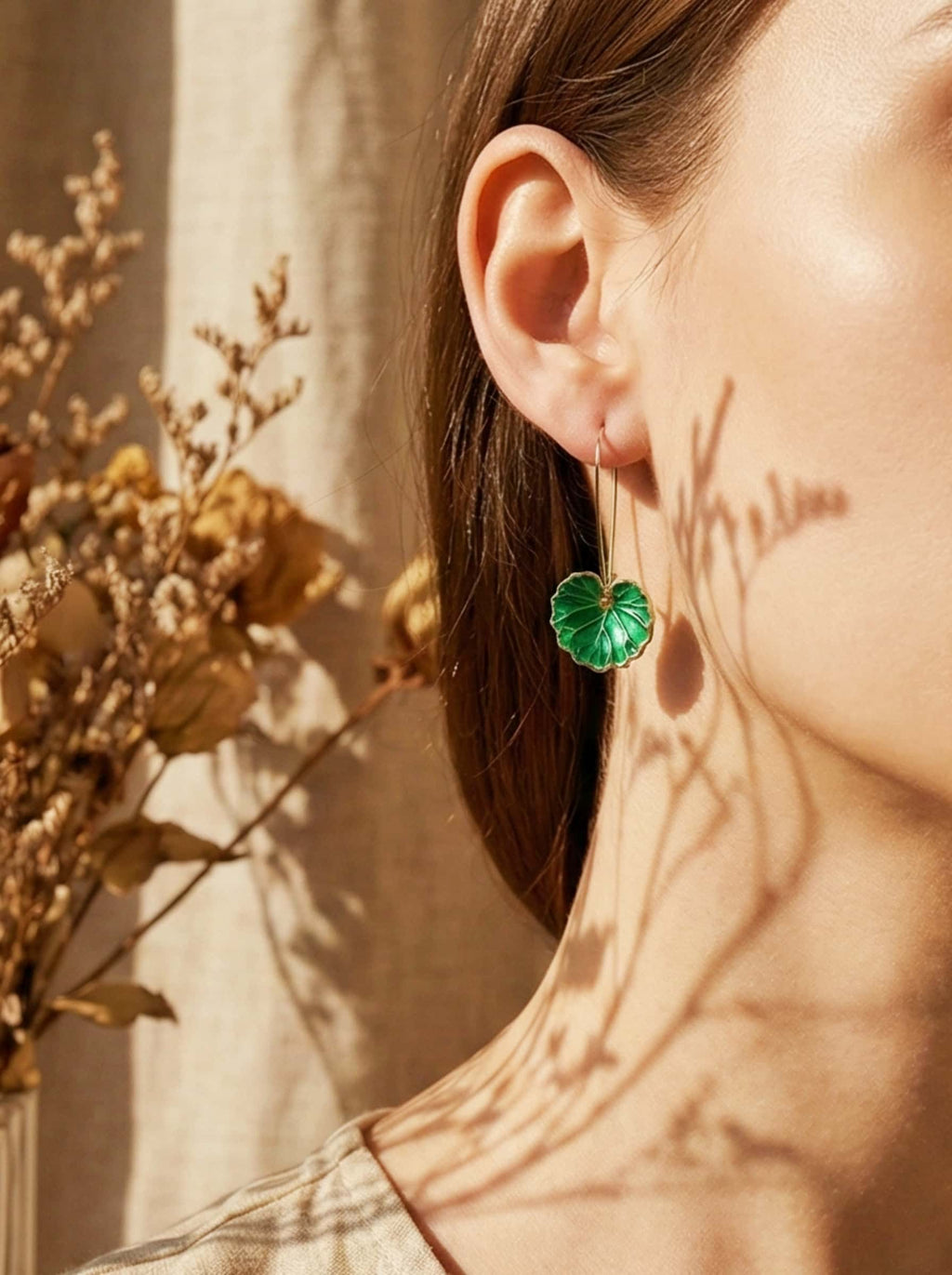 Close-up of a person wearing green leaf-shaped earrings with a blurred background