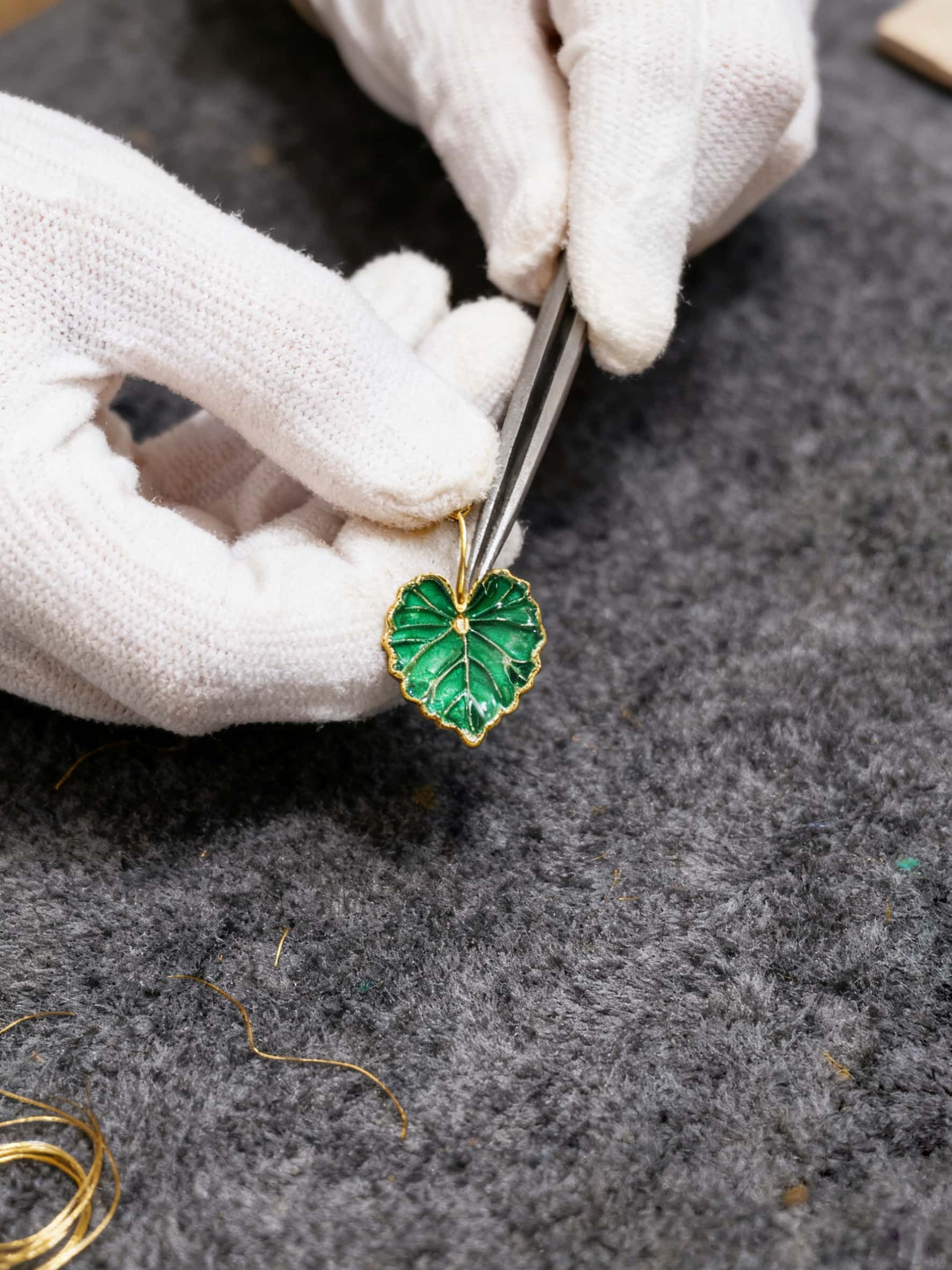 Jewelry making process with a green leaf-shaped pendant and tweezers on a gray surface.