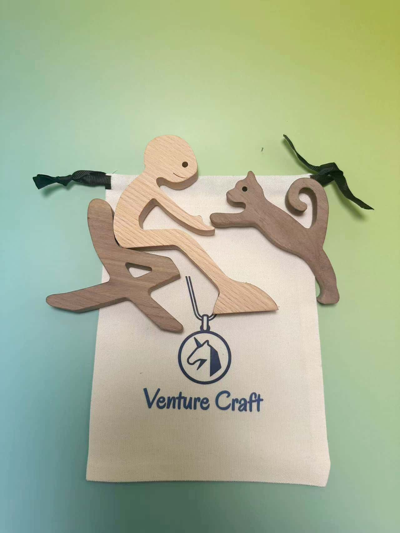 Handcrafted human and cat wood sculpture laid out on a premium canvas gift bag.