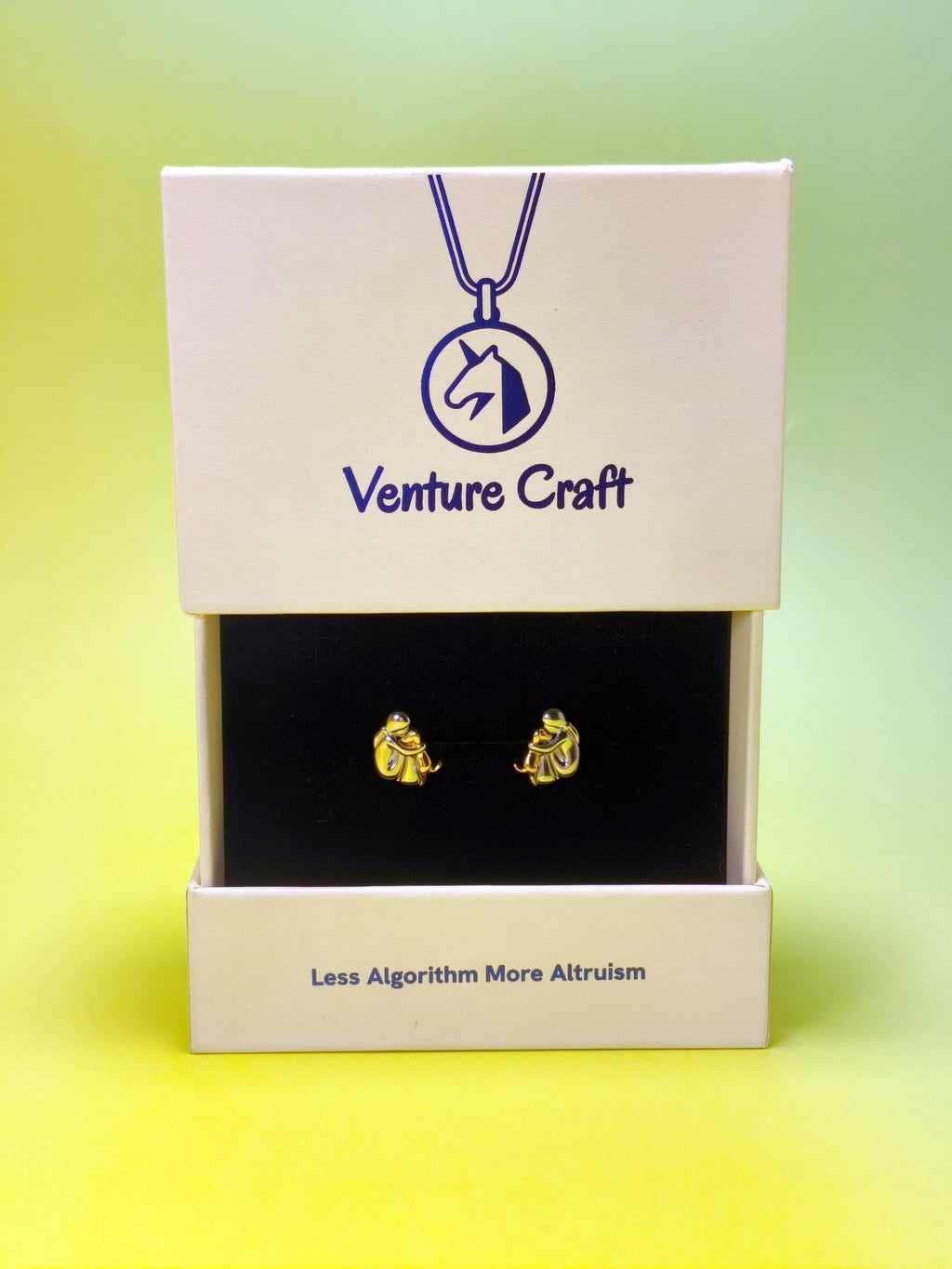 Gold human hug dog earrings in a Venture Craft box on a gradient background