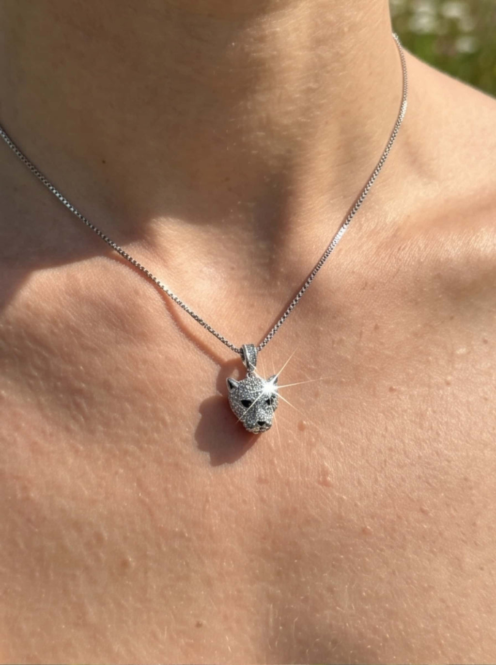 Close-up detail of the rhodium-plated leopard necklace pendant gleaming under natural golden sunlight, showcasing intricate gemstone settings