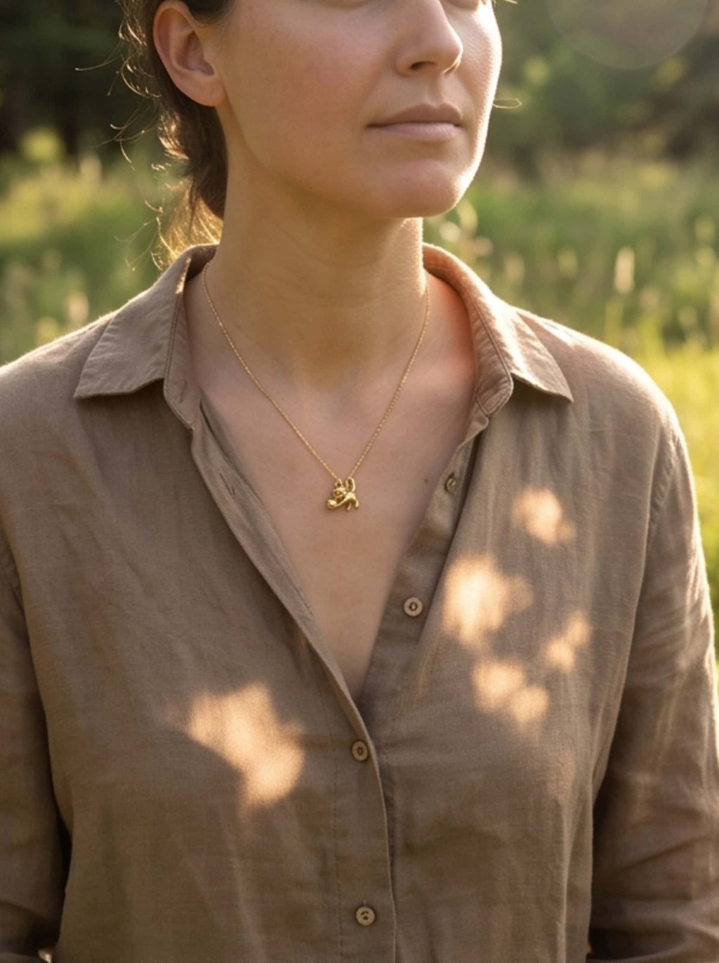 Outdoor lifestyle portrait of a woman wearing an everyday 18K gold cat pendant necklace with a neutral linen shirt
