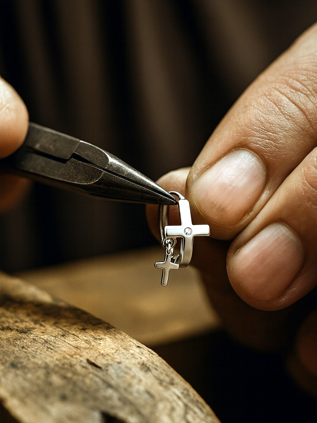 Close-up of hands using pliers to manipulate a silver cross pendant.