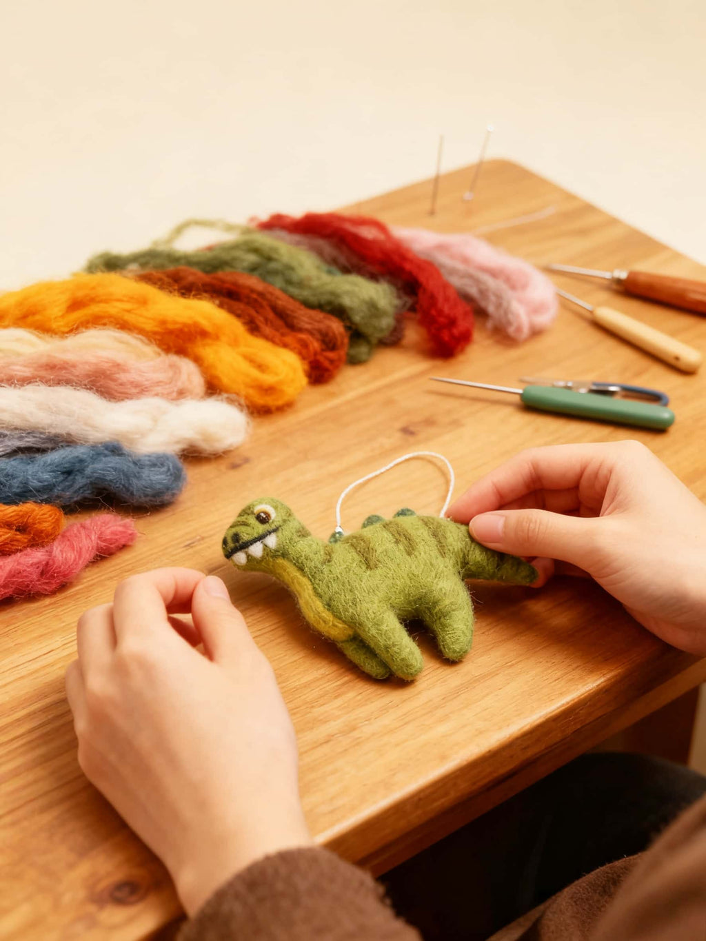Handmade green wool felt ornament dinosaur  on a wooden table with colorful yarn and knitting tools.
