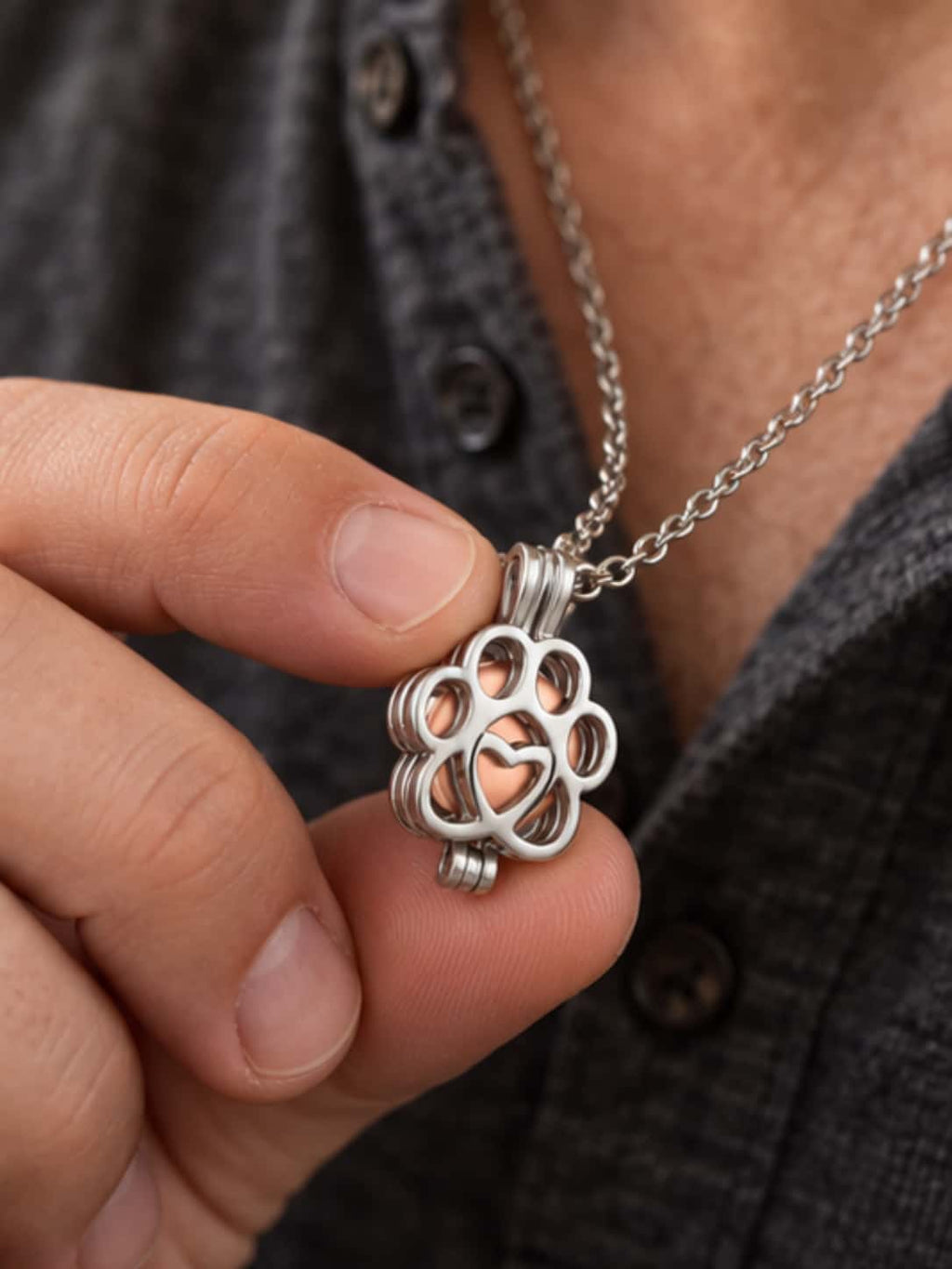 Close-up of a man holding the 316 stainless steel paw print necklace urn with rose gold inner chamber