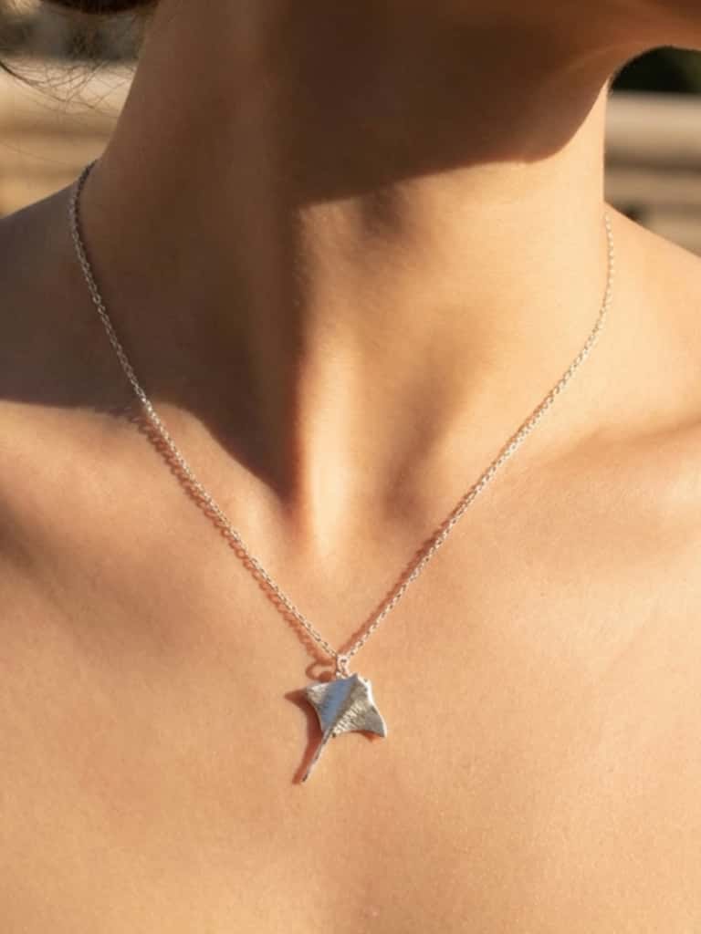 manta ray jewelry on a person's neck with a blurred background