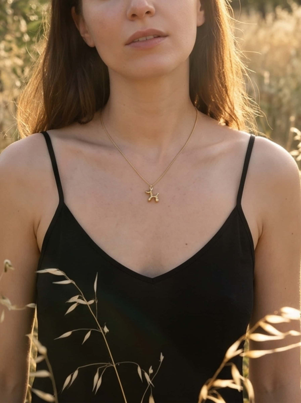 Mid-shot of a woman showcasing the elegant and whimsical 18K gold plated dog necklace in a serene, natural outdoor setting