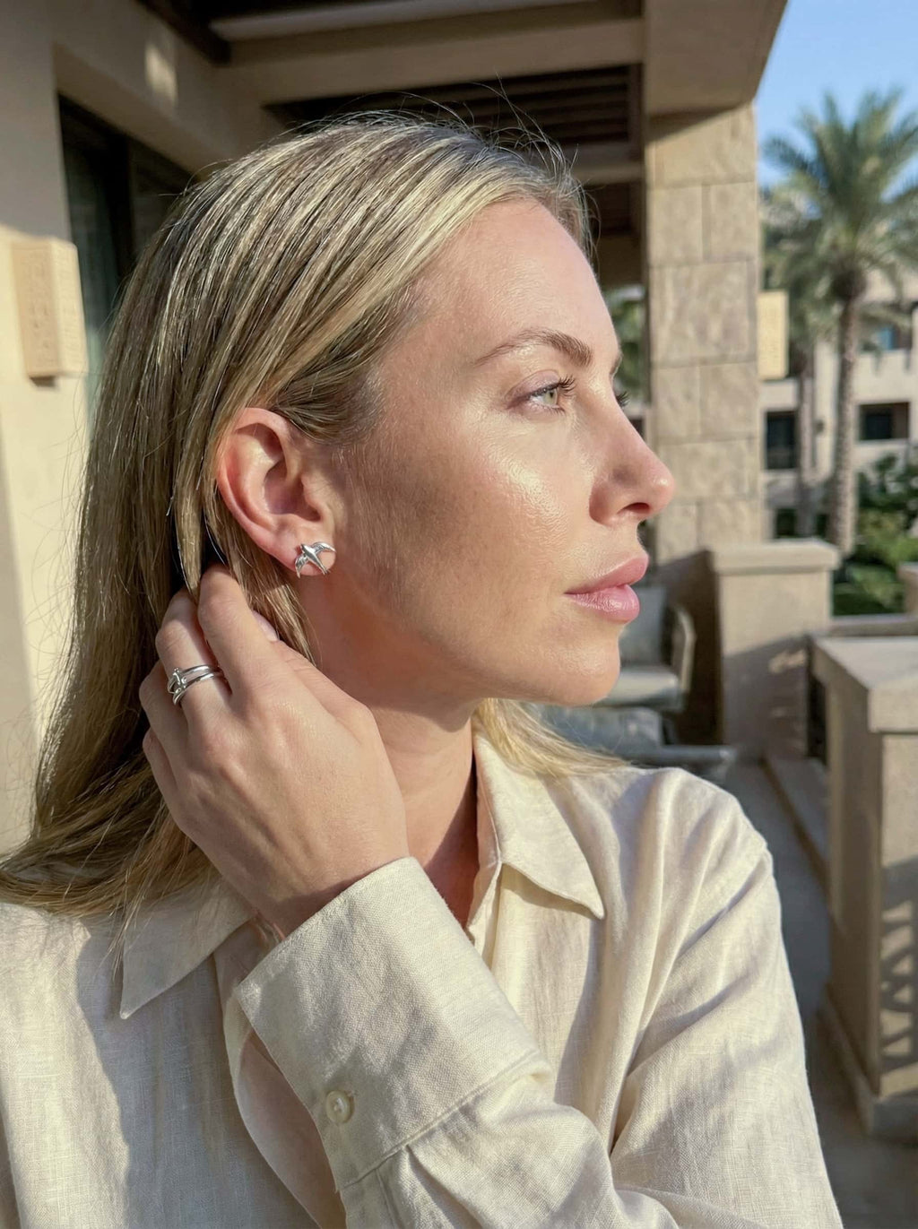 Woman adjusting an bird studs outdoors with a building and palm tree in the background