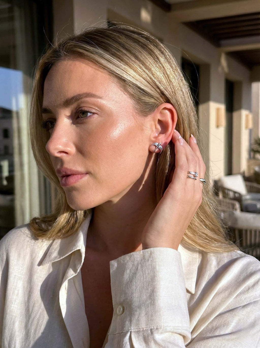 Woman wearing bird studs and a ring, with a blurred outdoor background