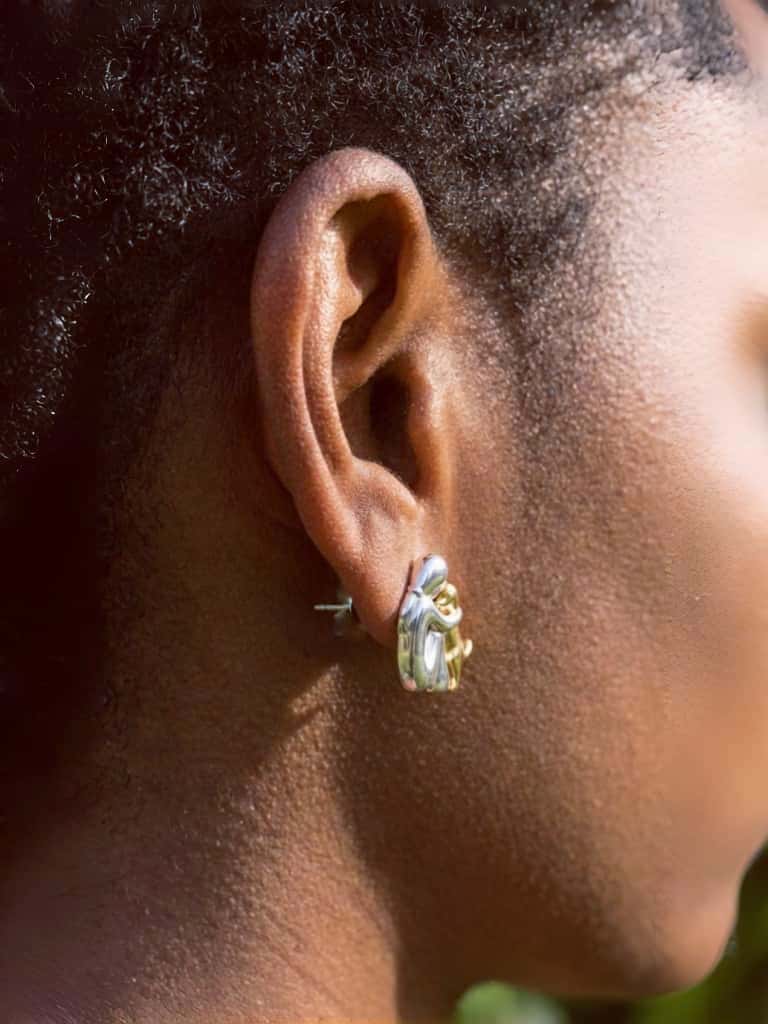 Close-up of an ear wearing a gold dog hug earring with a blurred background