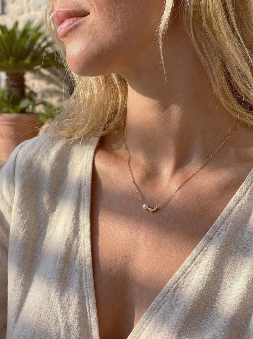 Close-up of a person wearing a delicate gold necklace with a small dolphin pearl pendant.