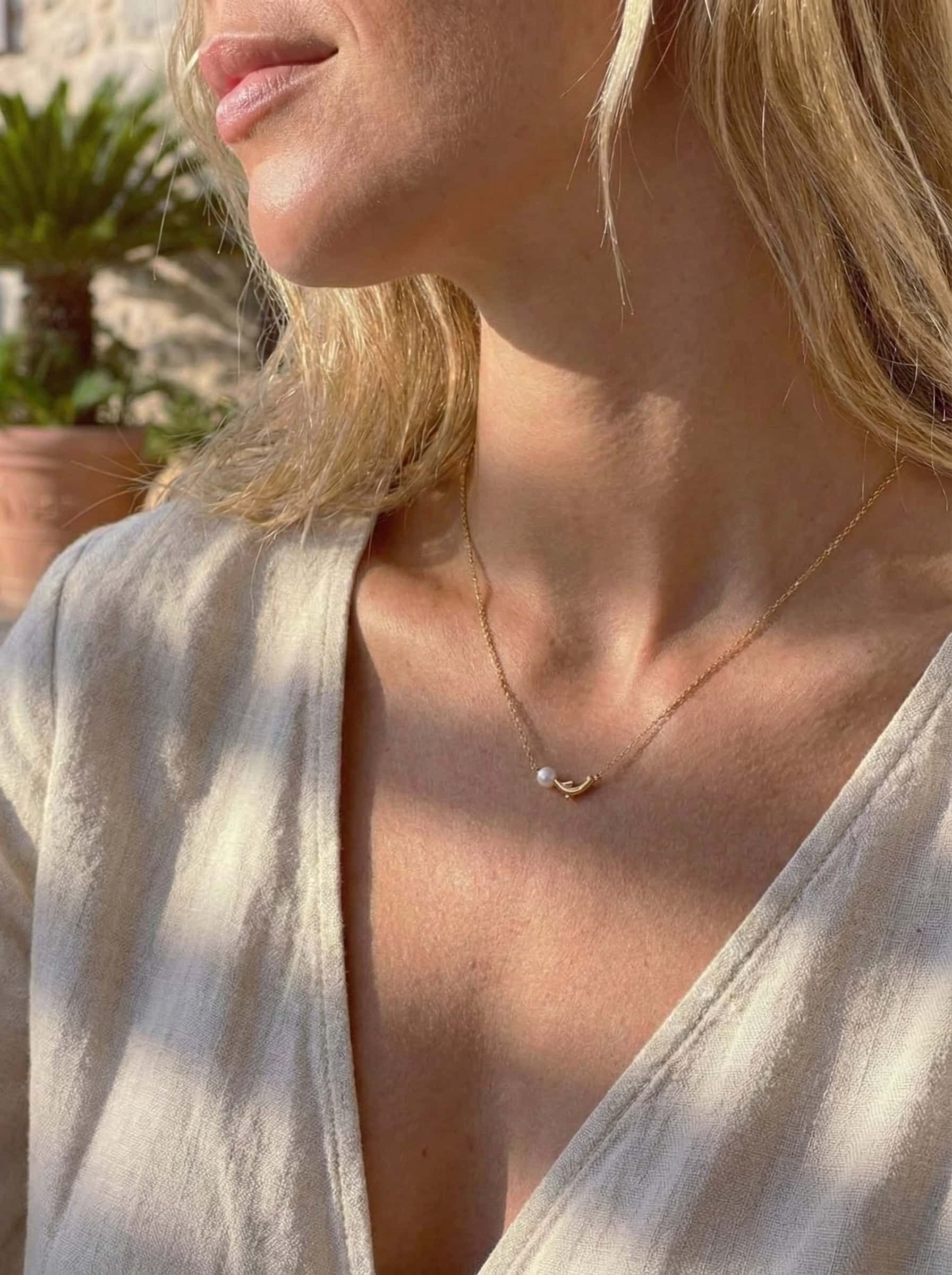 Close-up of a person wearing a delicate gold necklace with a small dolphin pearl pendant.