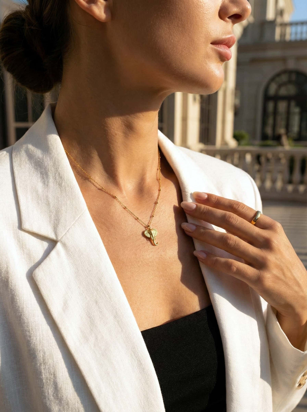 Woman wearing a gold elephant-shaped necklace with a building in the background