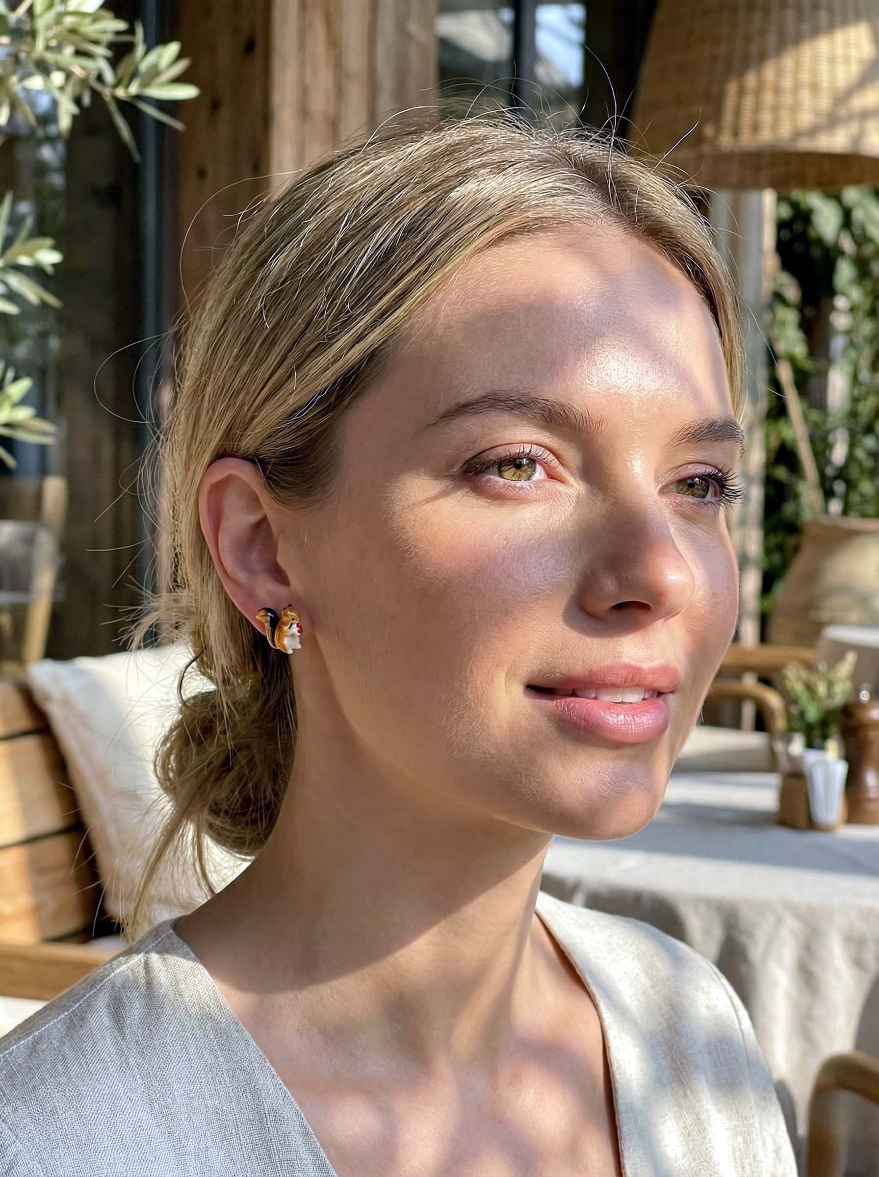 Woman with a casual hairstyle outdoors, wearing squirrel earrings.