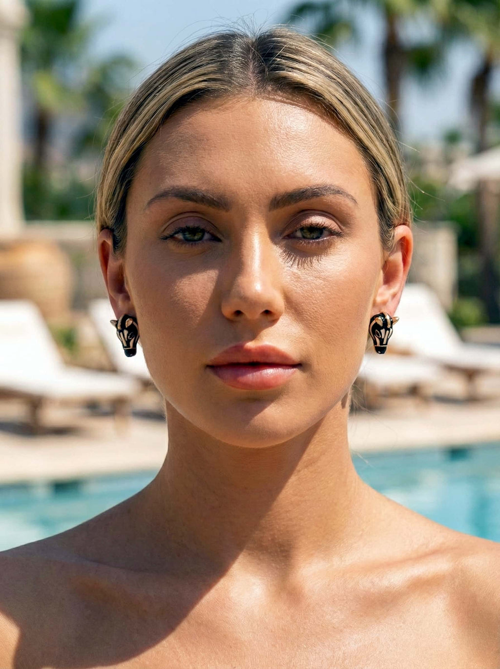 Woman with blonde hair and zebra-shaped earrings standing by a pool with blurred background