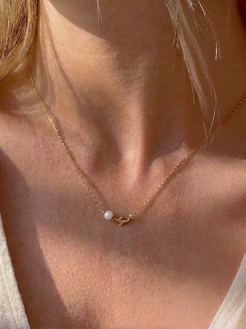 Close-up of a gold necklace with a pearl and dolphin pendant on a person's neck.