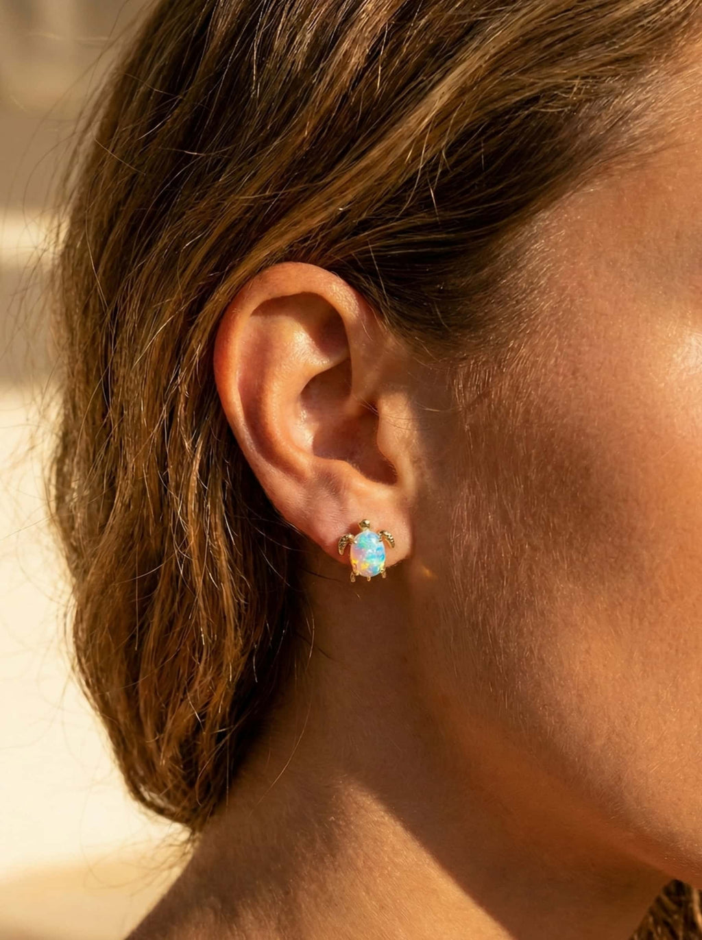 Close-up of an ear wearing a turtle gold earring with a opal gemstone.
